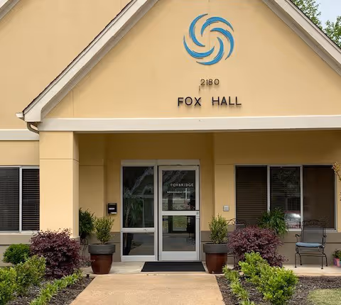 You see the entrance to Fox Hall senior living facility with glass doors and potted plants.