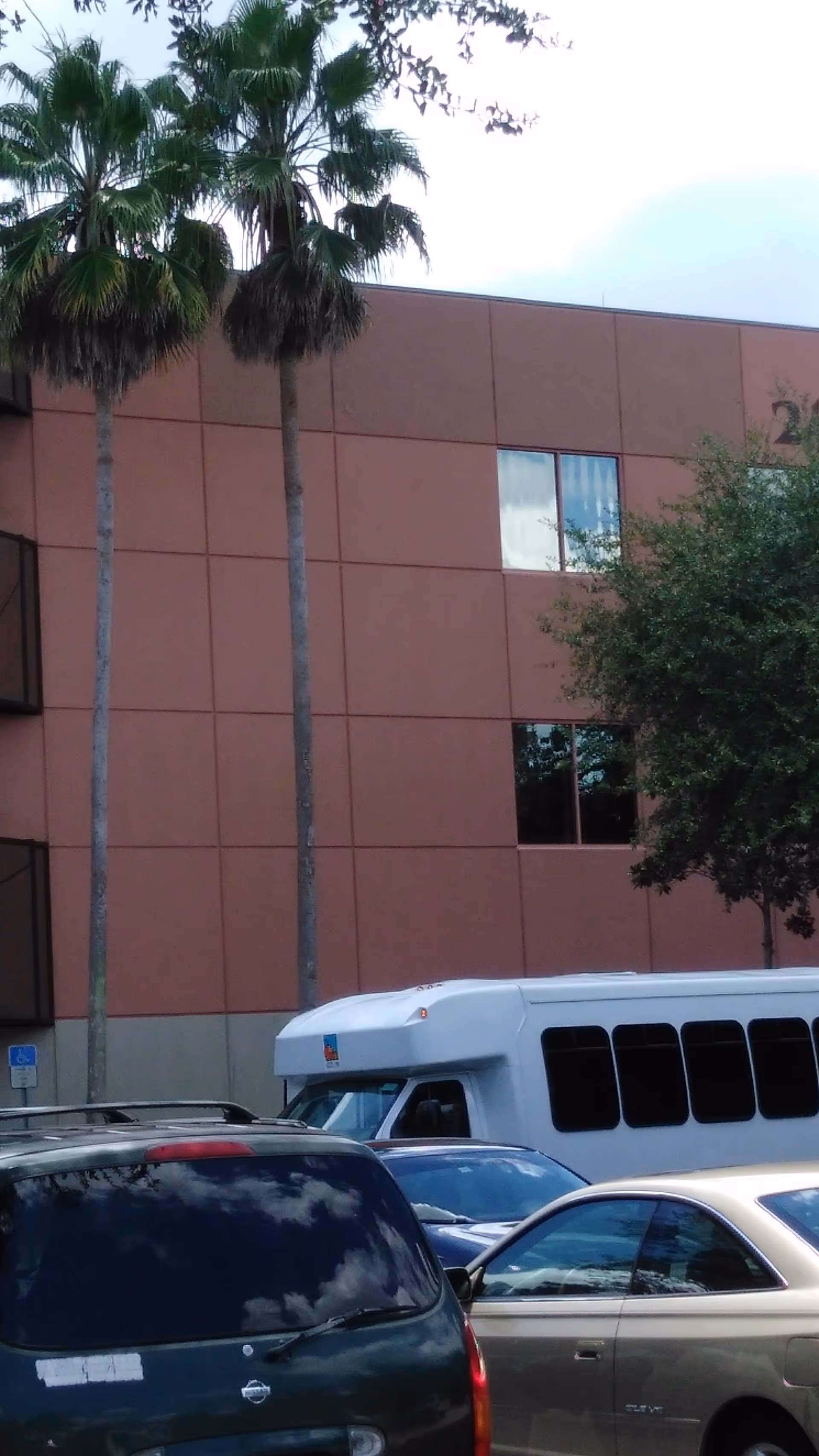 Exterior view of a brown Park Place Surgery Center building with palm trees and parked shuttle.