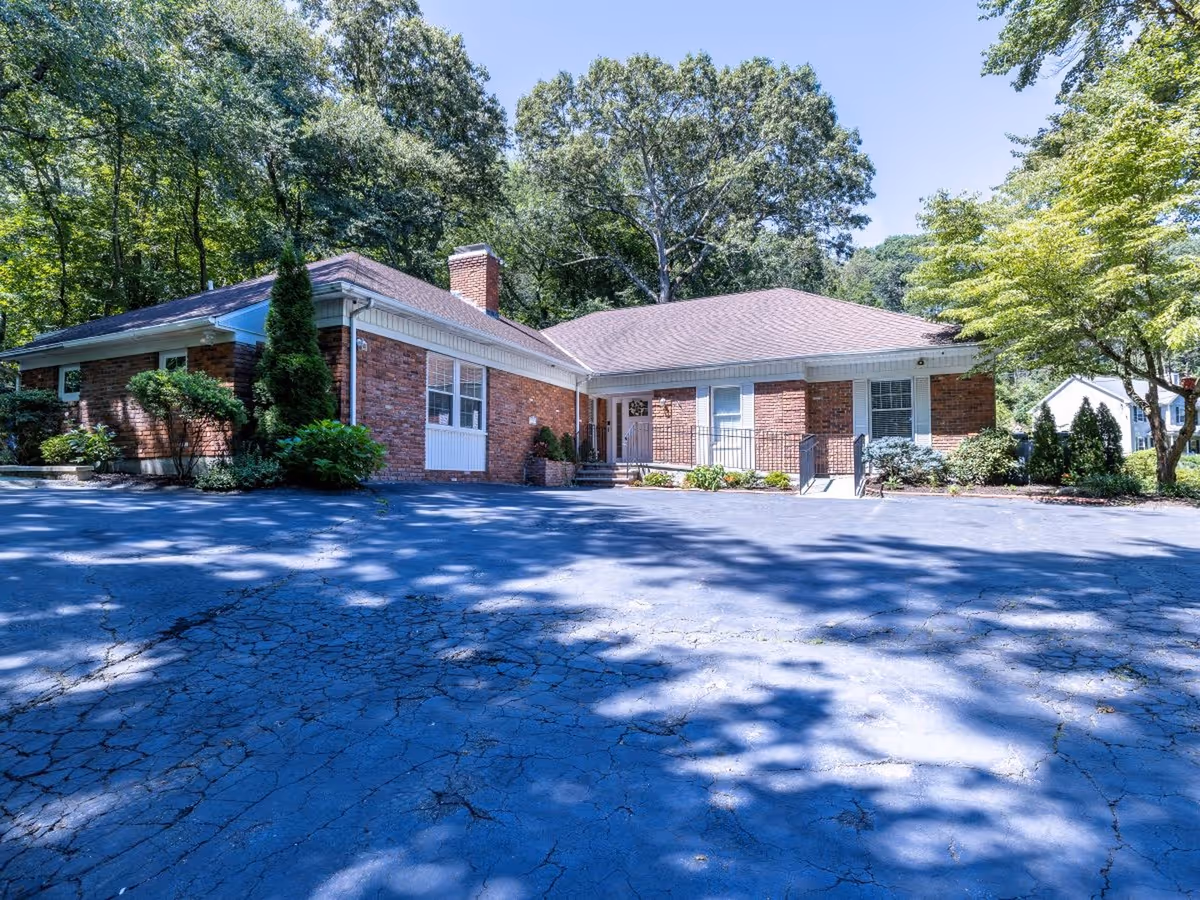 Brick, single-story senior living building with front entrance, surrounded by trees and a parking lot.