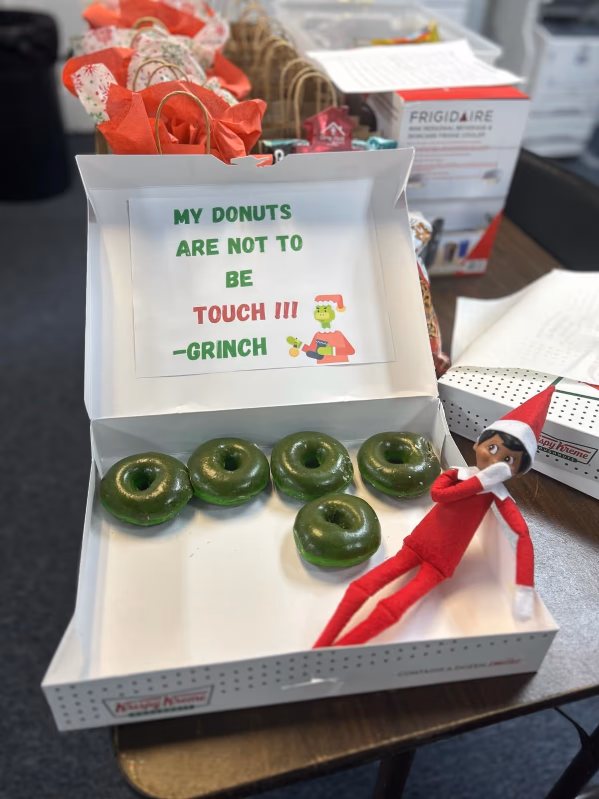 Box of green donuts with a small elf figure and a sign about not touching.