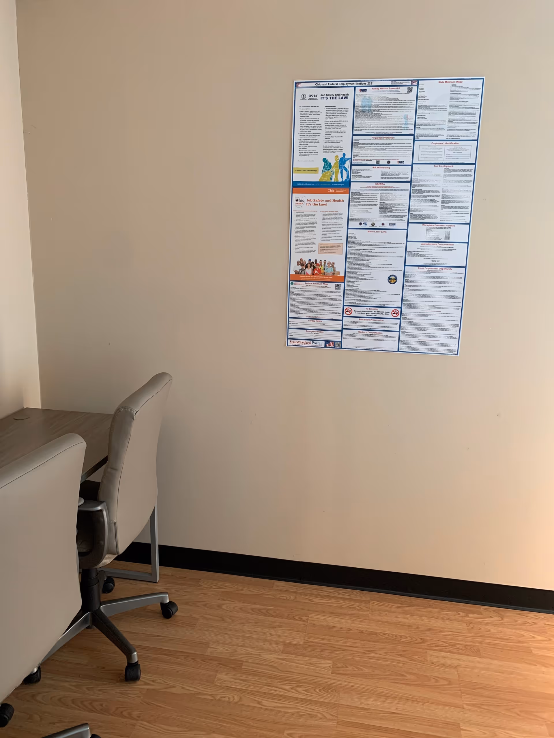 Office corner with chairs, desk, and a large informational poster on beige wall.