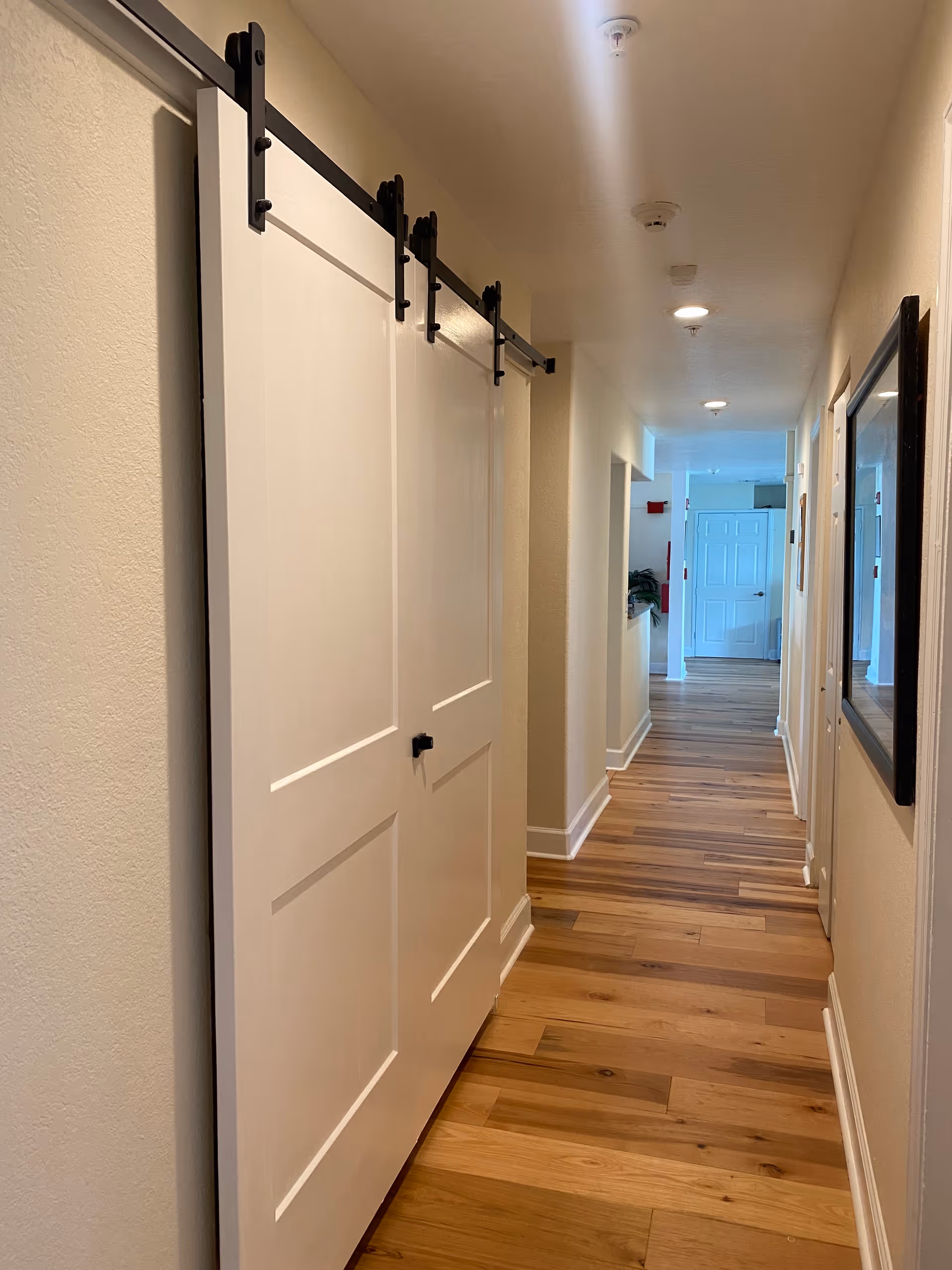 Long hallway in a senior living facility with white sliding doors and wood flooring.
