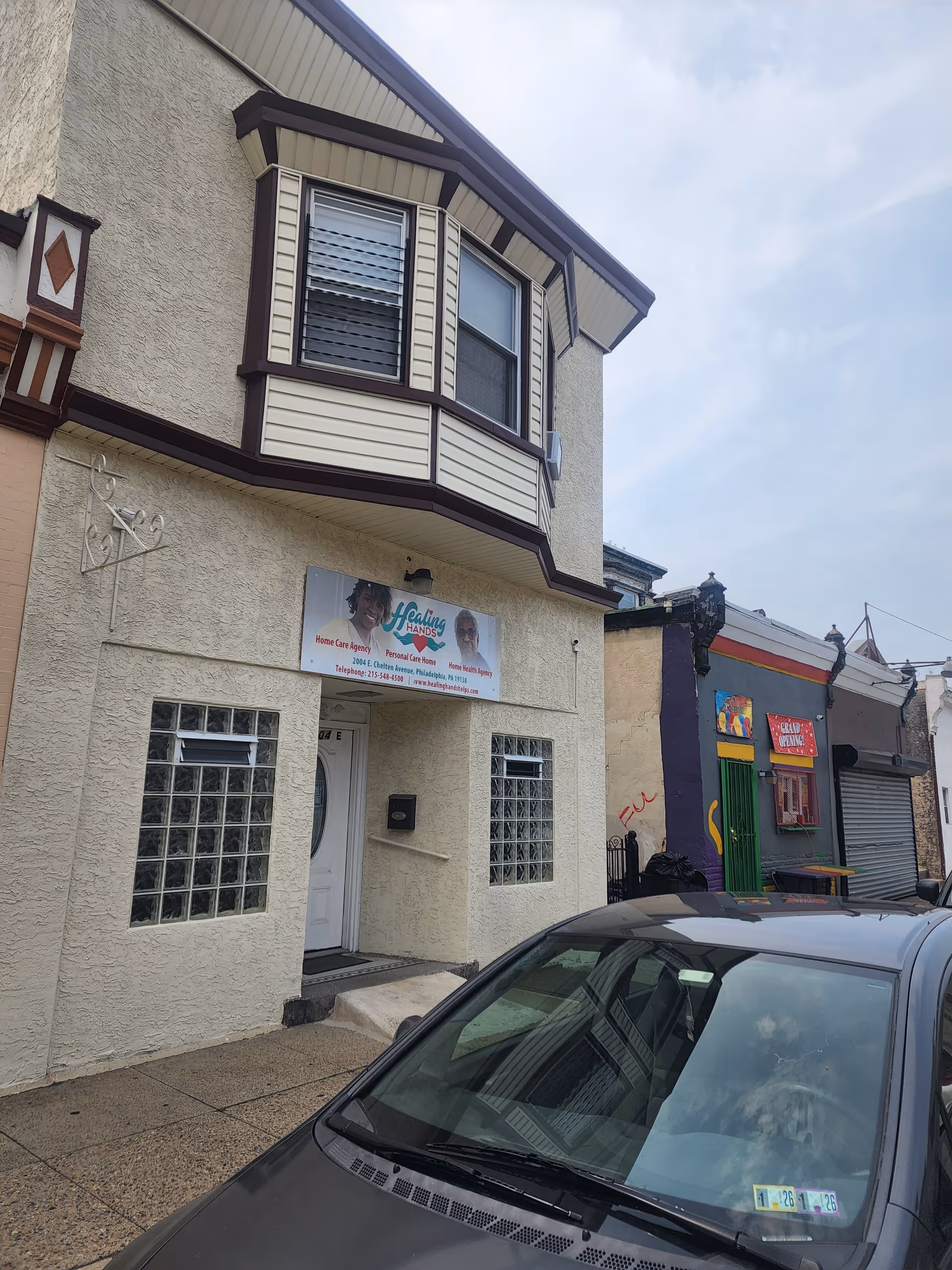 Two-story beige building with Healing Hands Helps sign, entrance doorway, and a car parked outside.