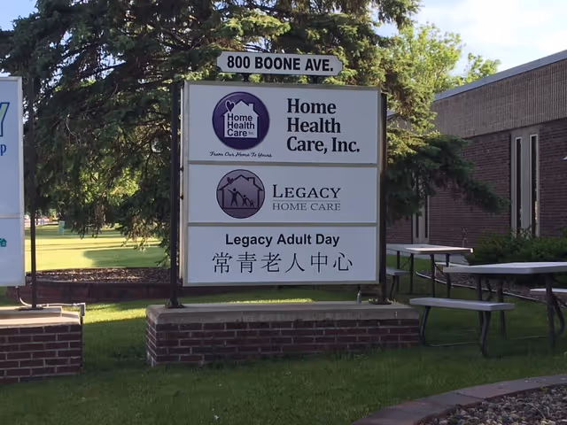 Outdoor sign for Legacy Home Care beside a brick building with a picnic table.