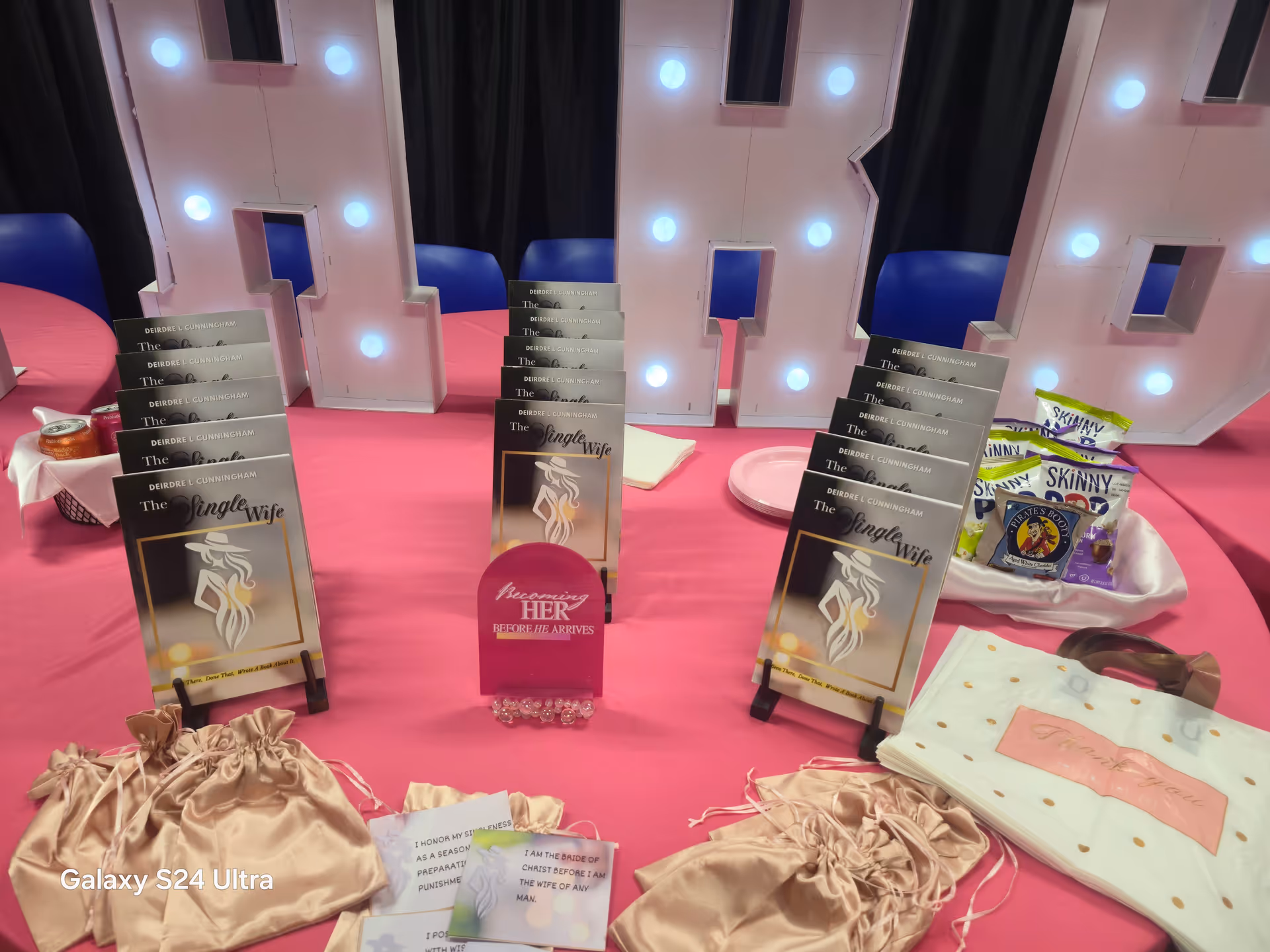 A pink display table holds The Single Wife books and event materials.