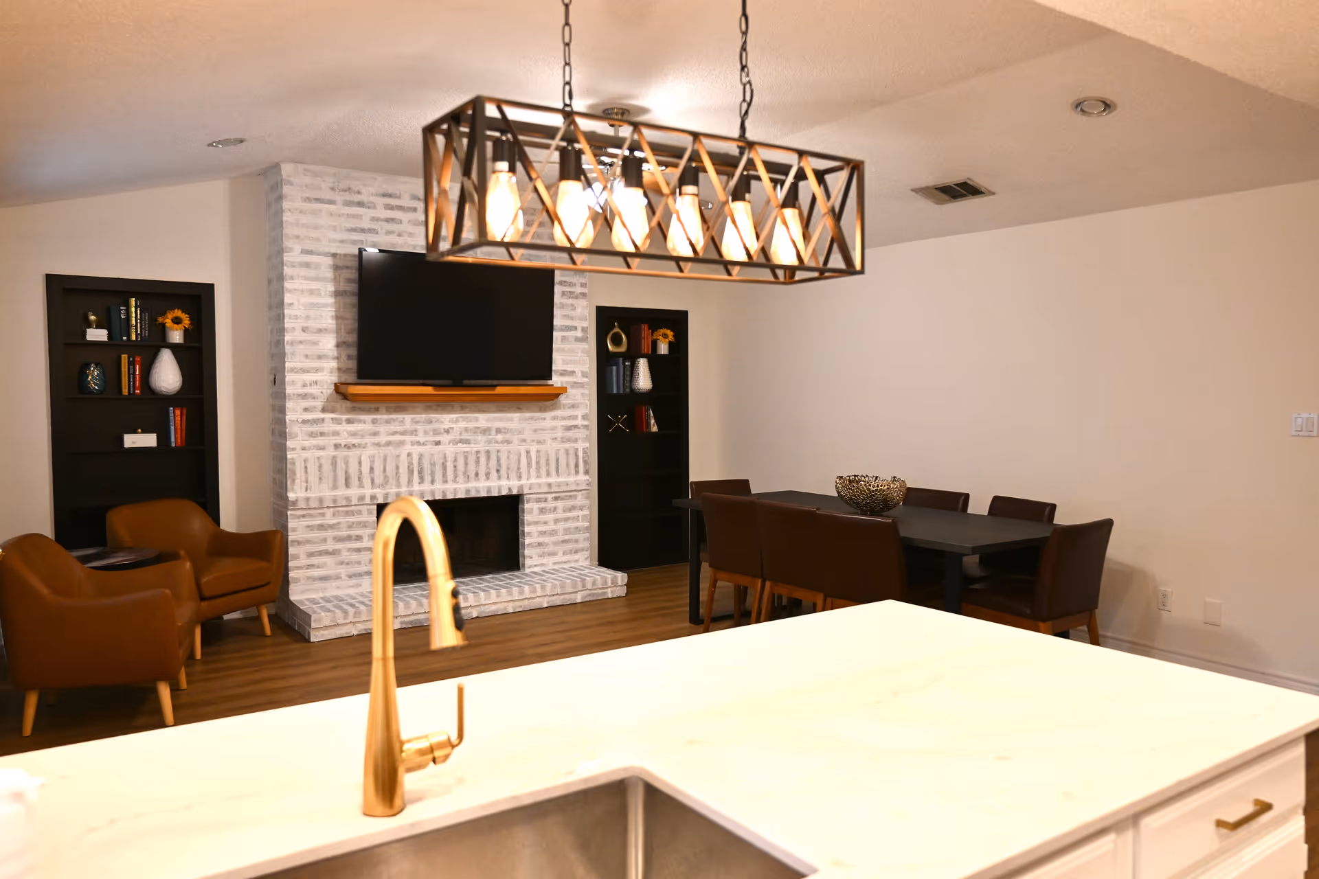 Bright interior common area with a brick fireplace, TV, bookshelves, and a dining table.