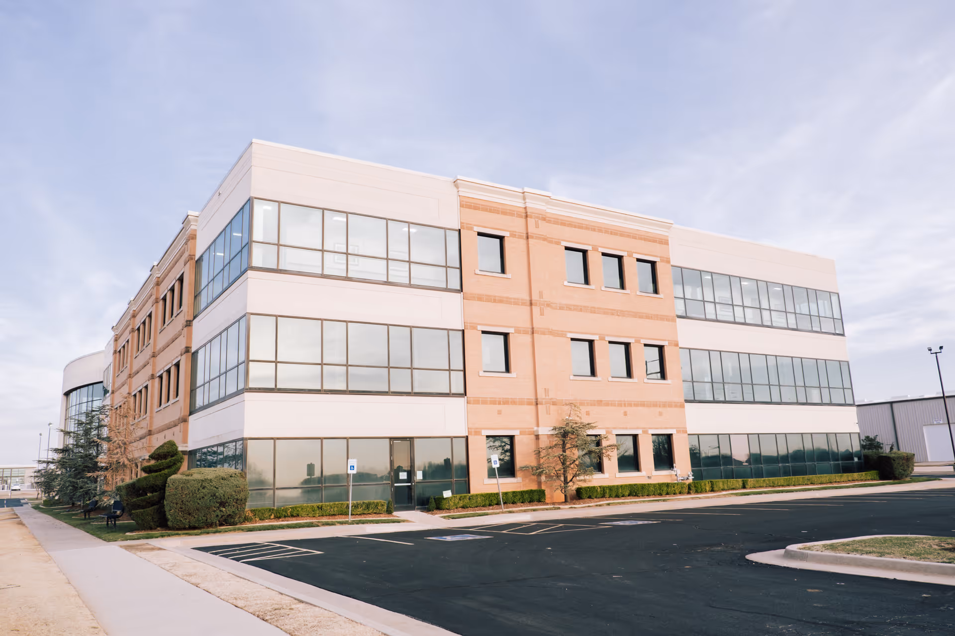 Three-story brick-and-glass building with large windows and a surrounding parking lot.