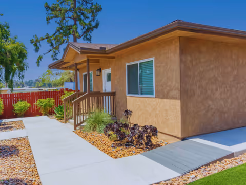 Exterior view of a beige single-story assisted living facility with a porch and landscaped walkway