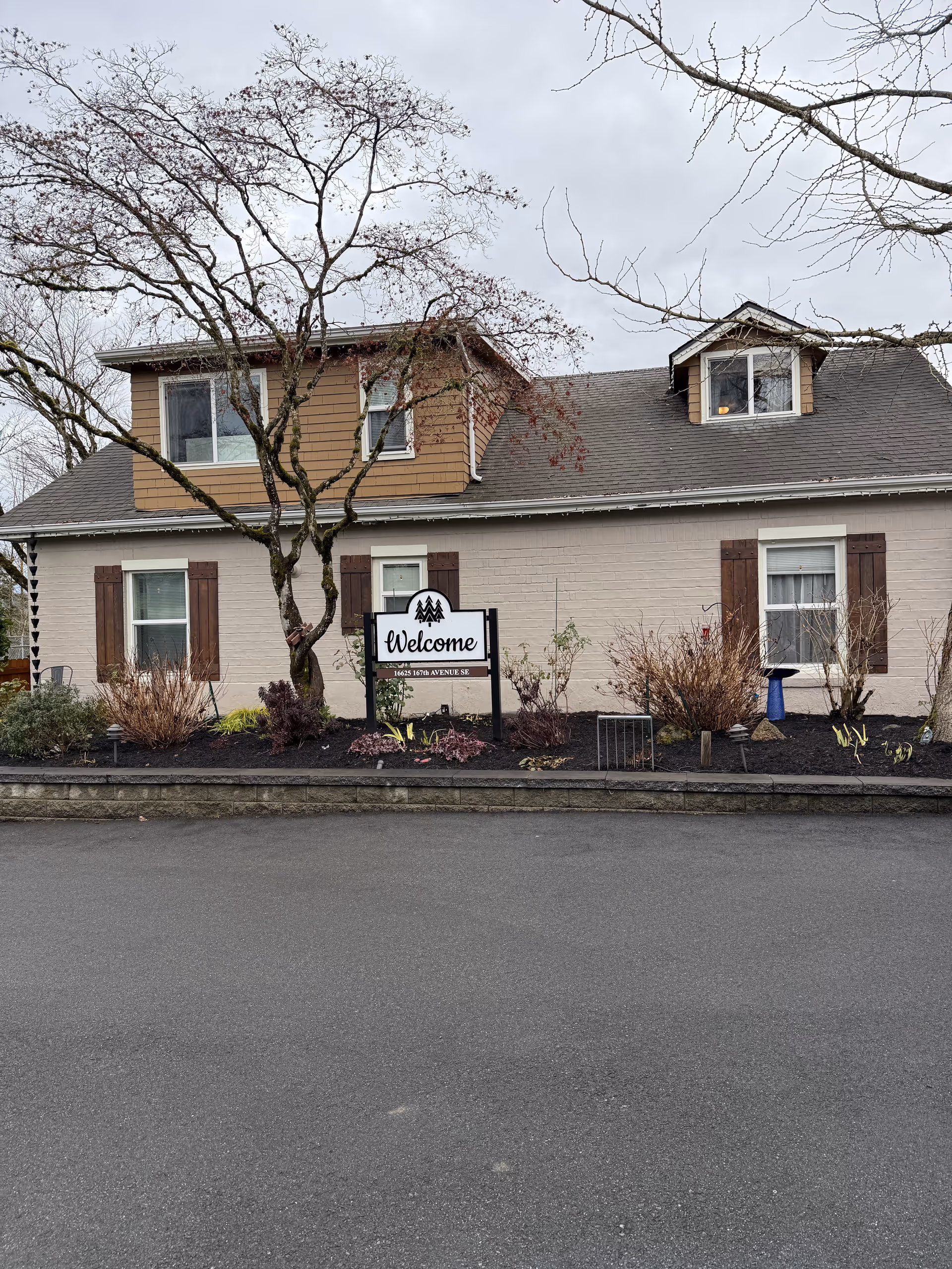 Front of a beige senior living building with a welcome sign and landscaped border.