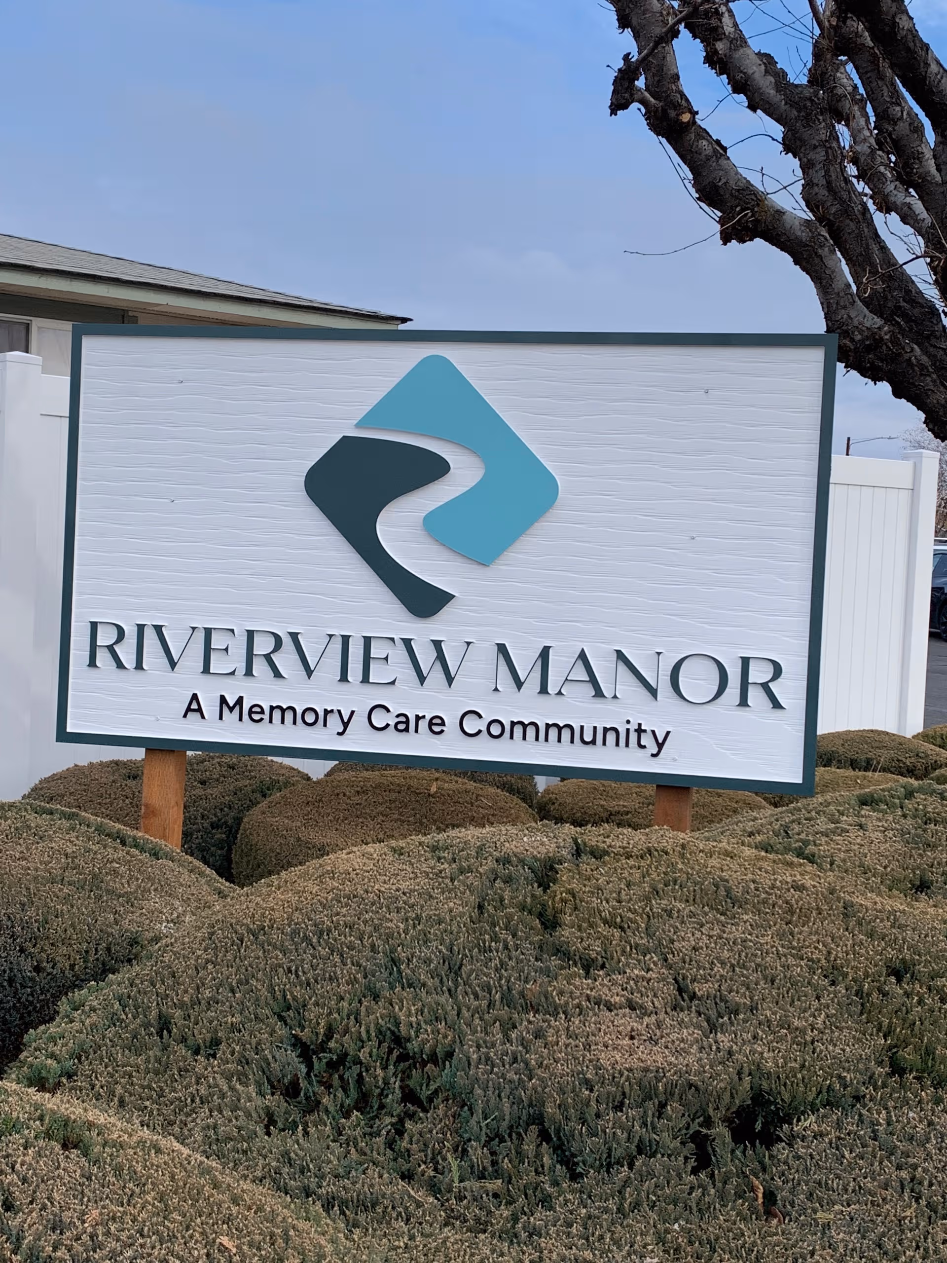 Riverview Manor sign in front of landscaped shrubs reads 'A Memory Care Community'.
