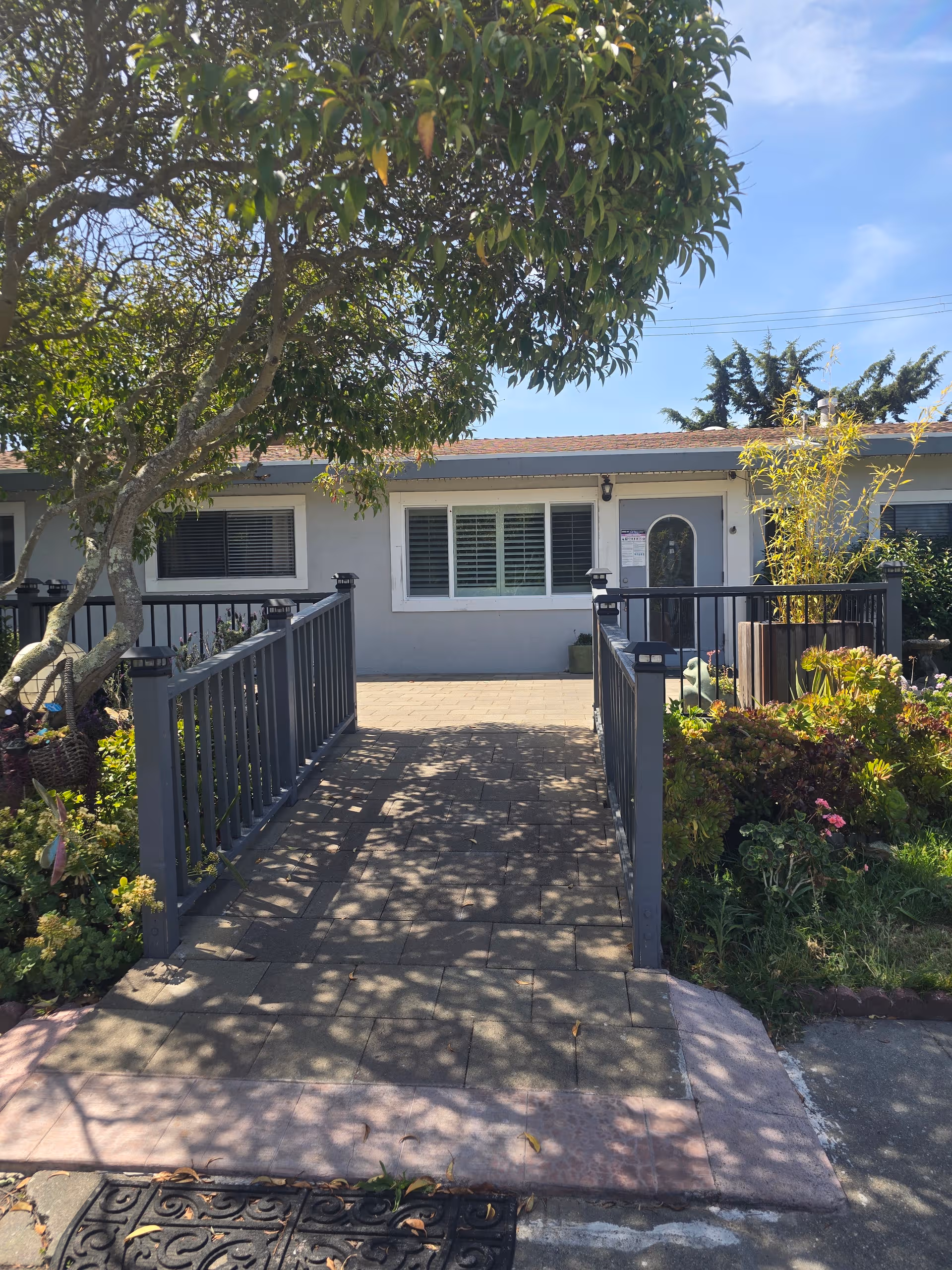 A paved walkway with railings leads to the front entrance of a single-story senior home.
