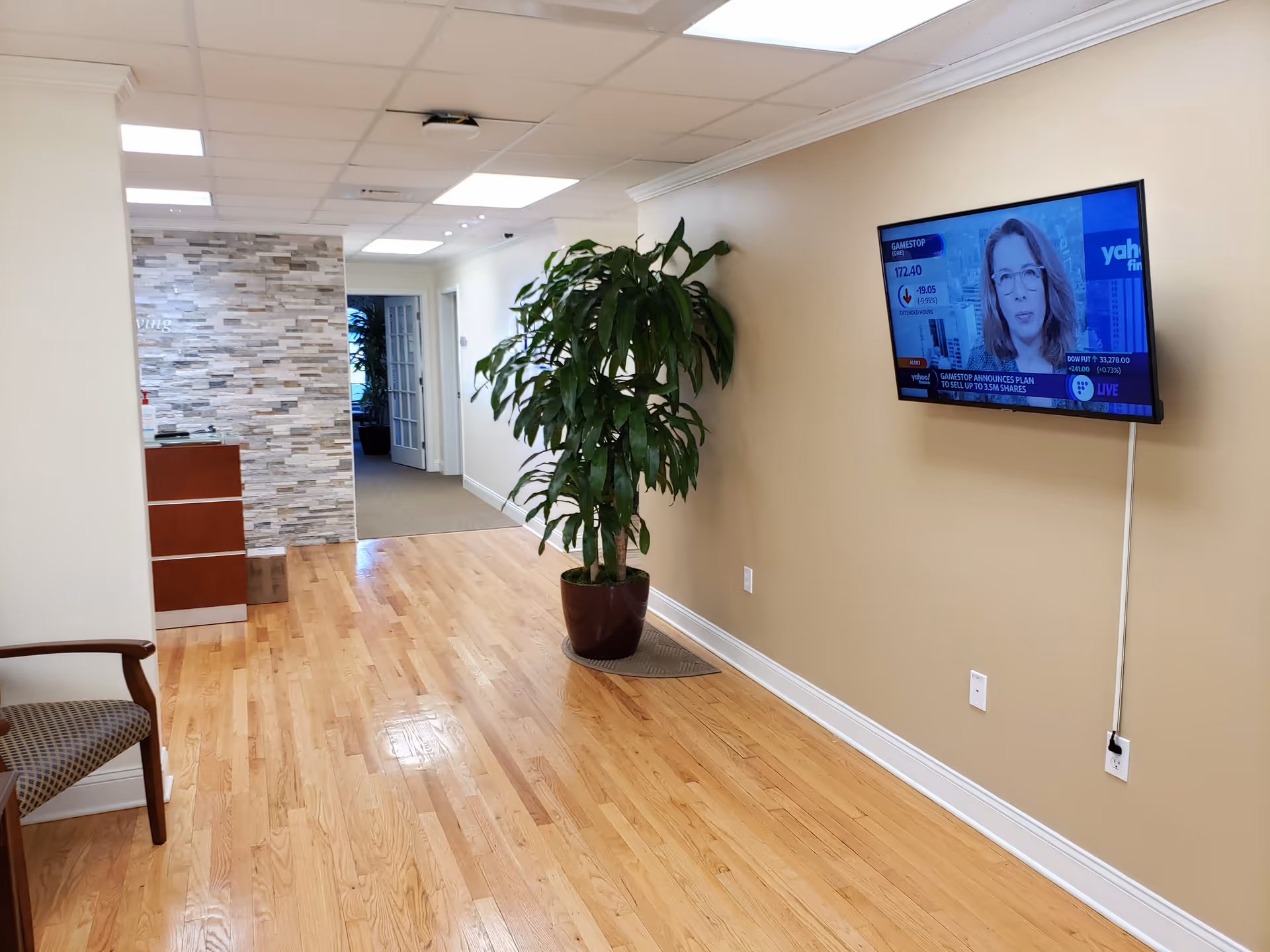 A hallway in a senior living facility with a large plant and a wall-mounted TV.