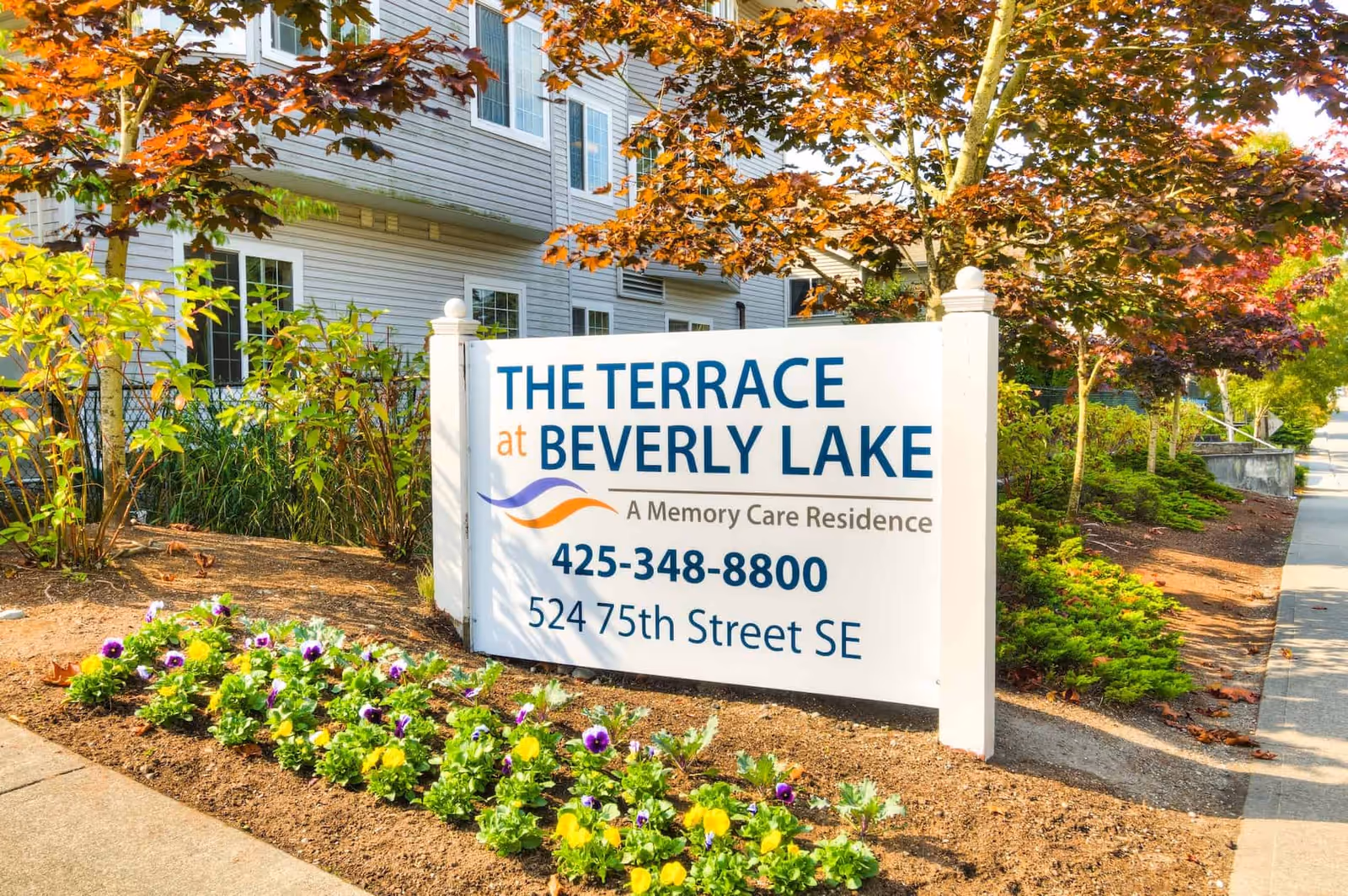 Outdoor sign for The Terrace at Beverly Lake in front of a residential building with landscaped flowers and trees.