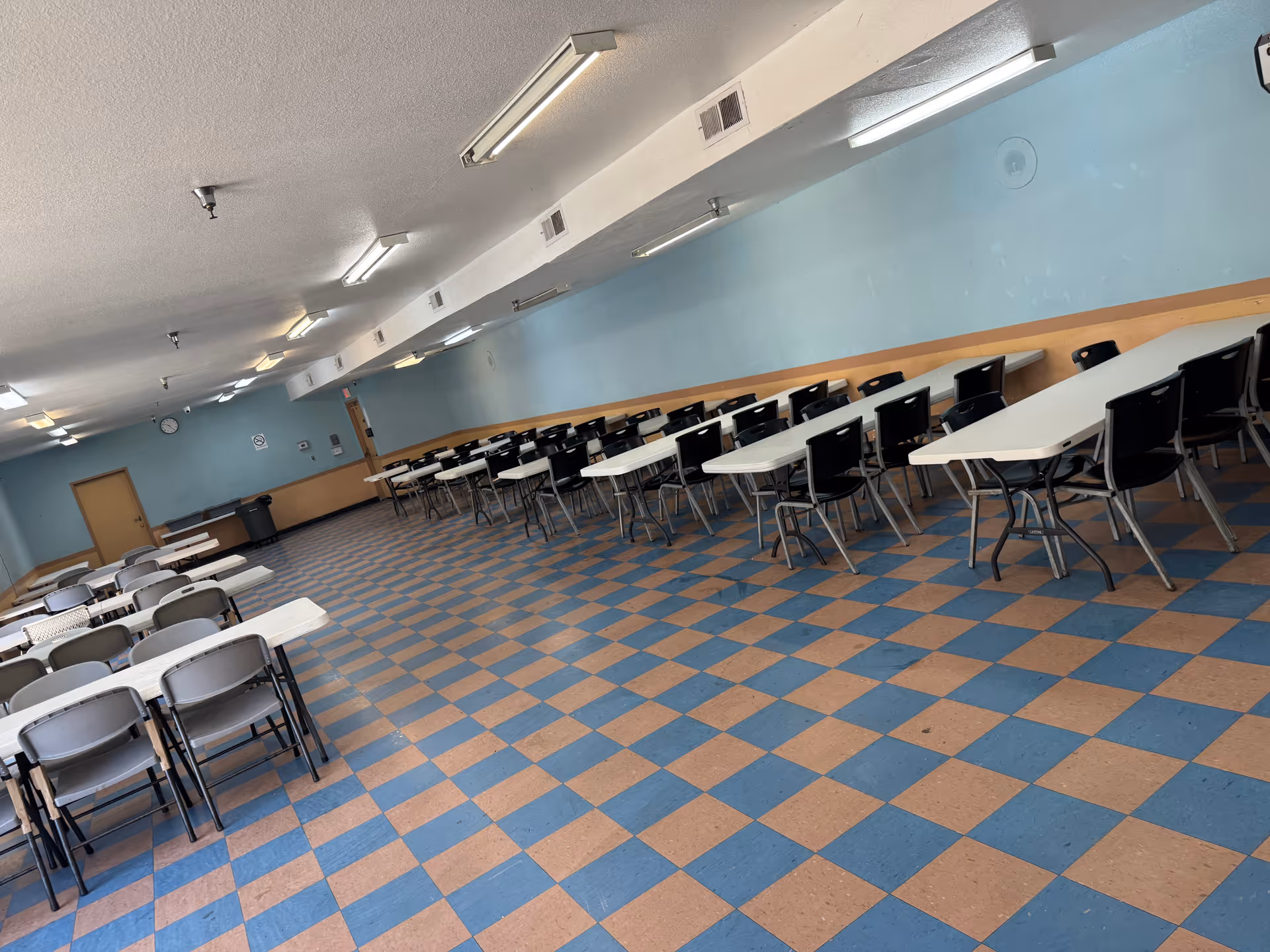 Empty Pico Rivera Gardens dining hall with rows of tables under fluorescent lights.