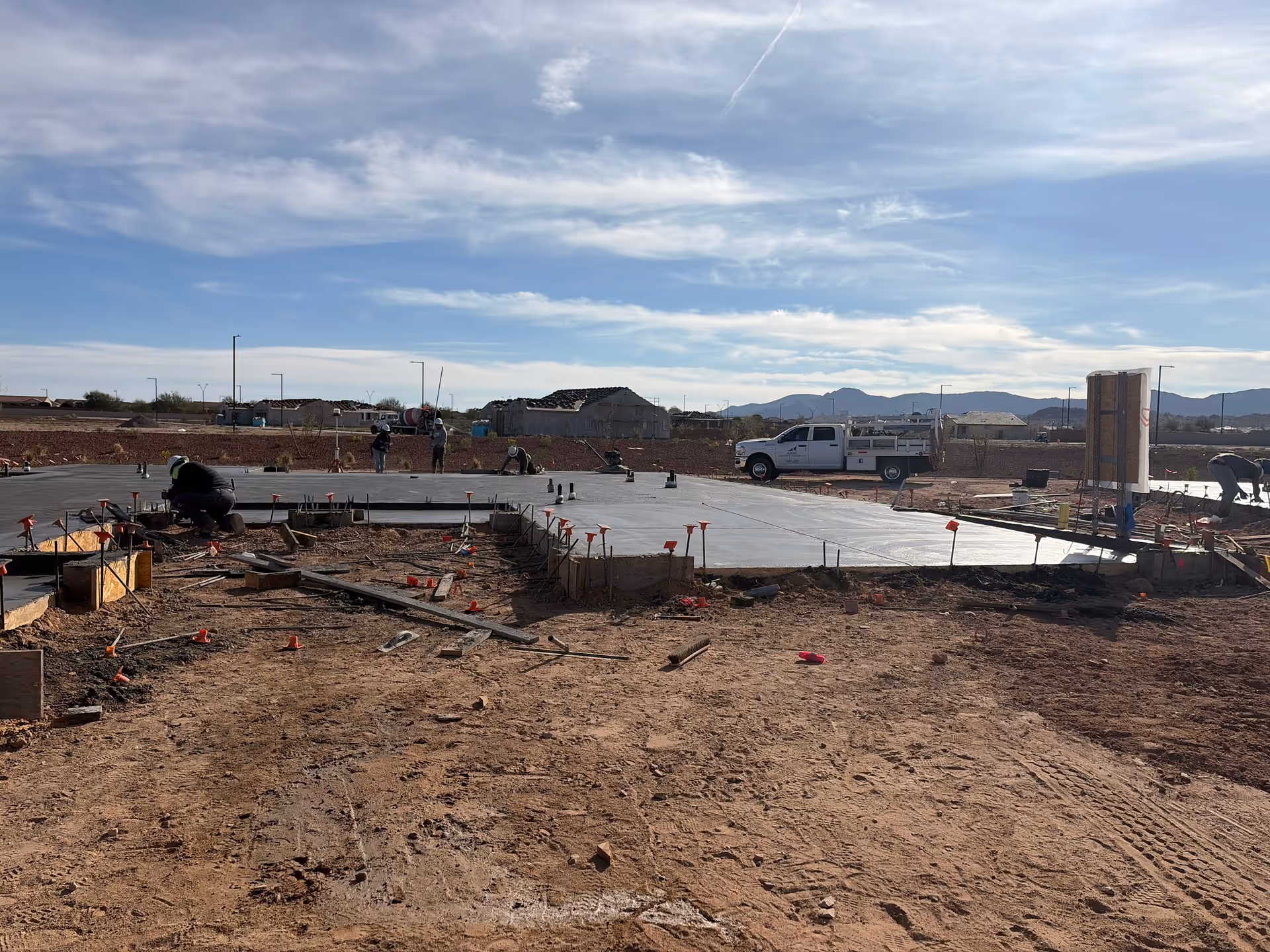 Outdoor construction site with workers laying a large concrete foundation.
