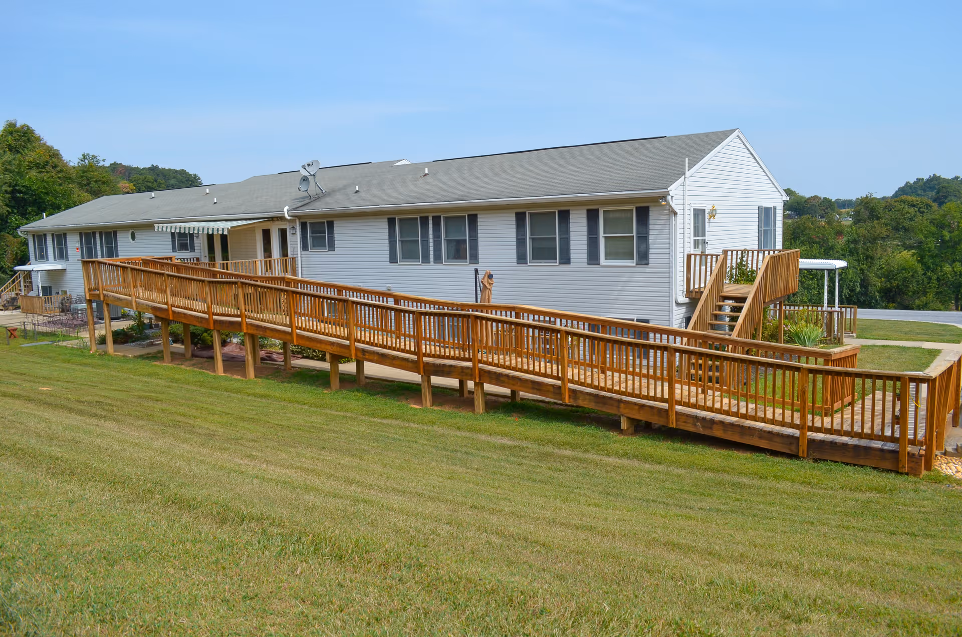 A single-story assisted living facility with a long wooden ramp along the grassy slope outside.