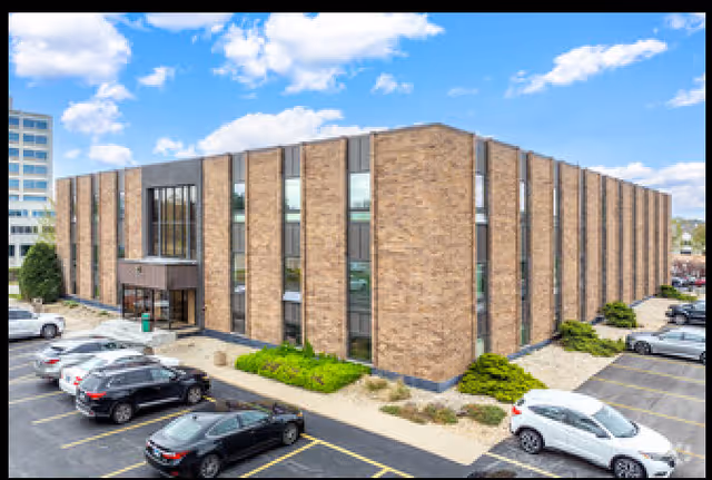 Exterior brick building with large windows, parking lot, and landscaped entrance.