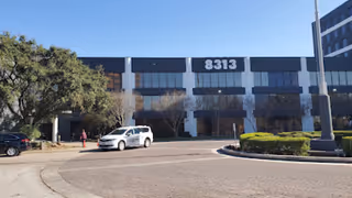 Front view of a commercial building labeled 8313 with parked cars and trees.