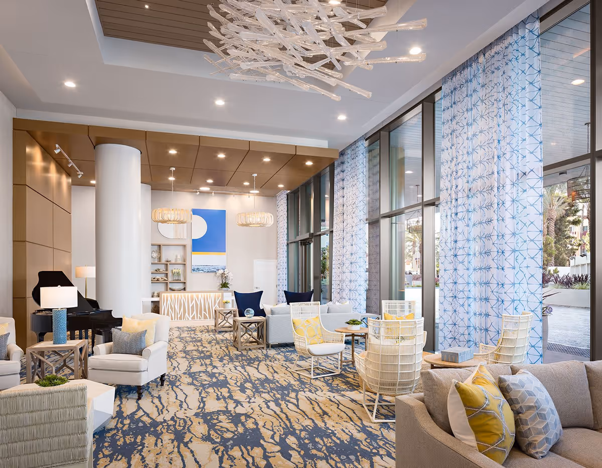 Spacious, brightly lit lounge with multiple seating areas, large floor-to-ceiling windows, patterned curtains, and contemporary decor.