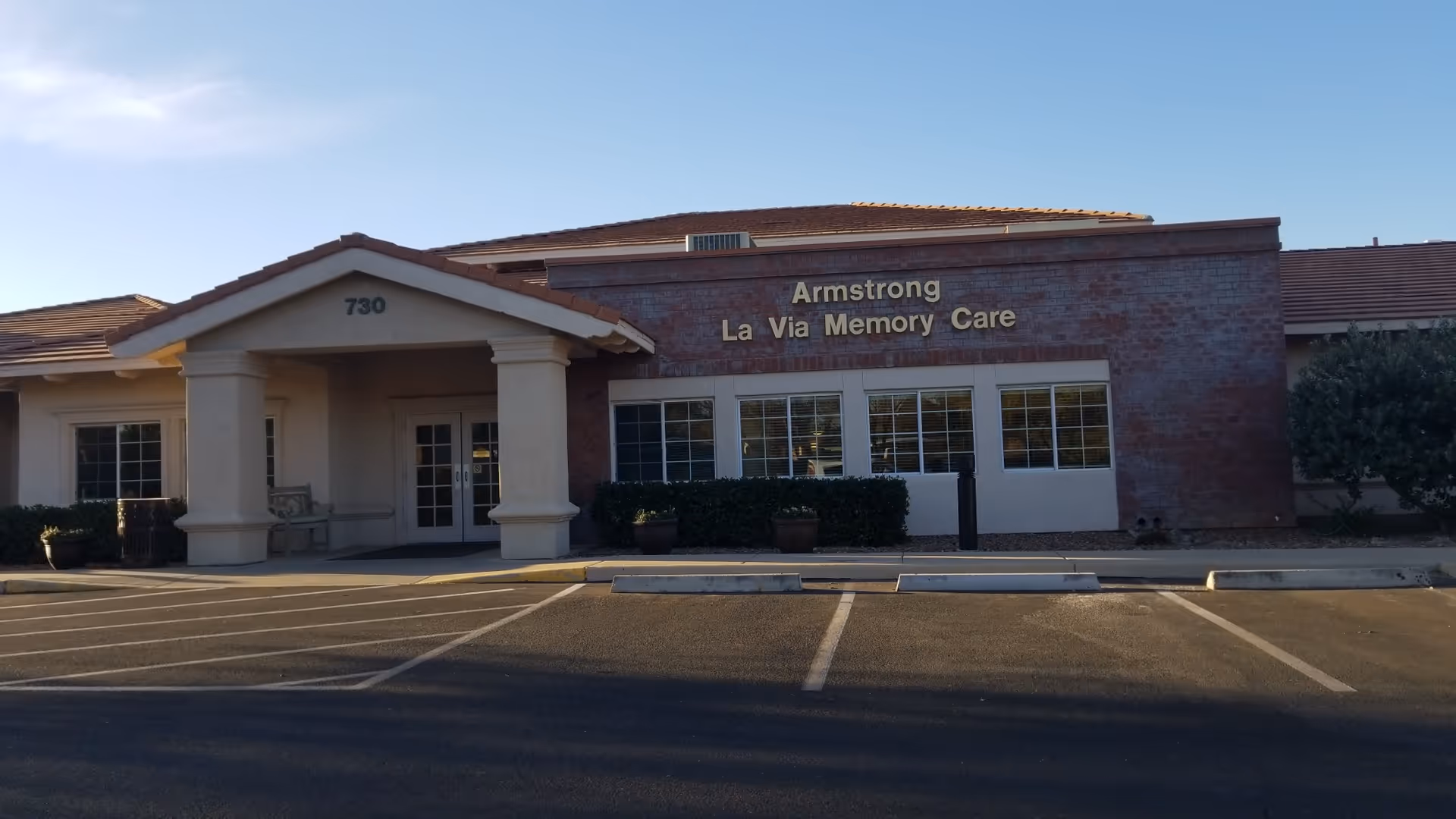 Front exterior of Armstrong La Via Memory Care building with a parking lot.