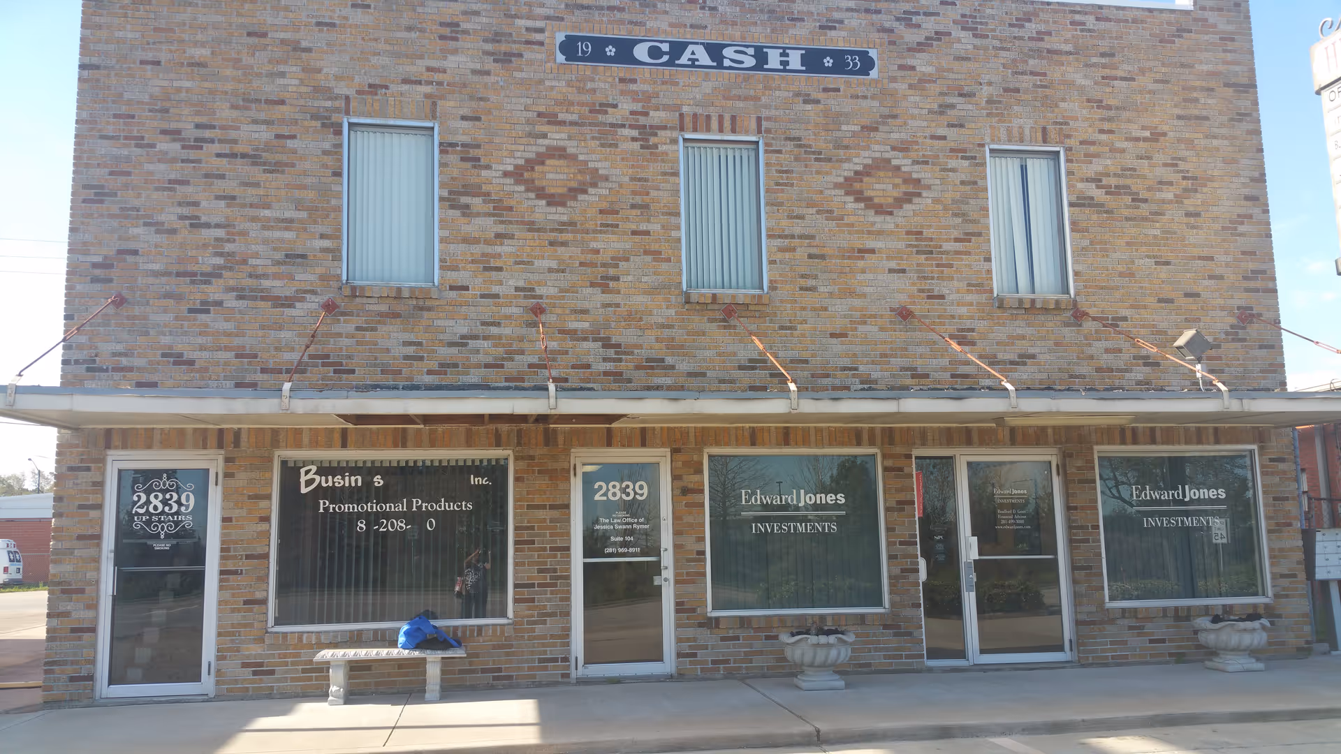 Brick storefront building with large windows and multiple signs along a sidewalk.