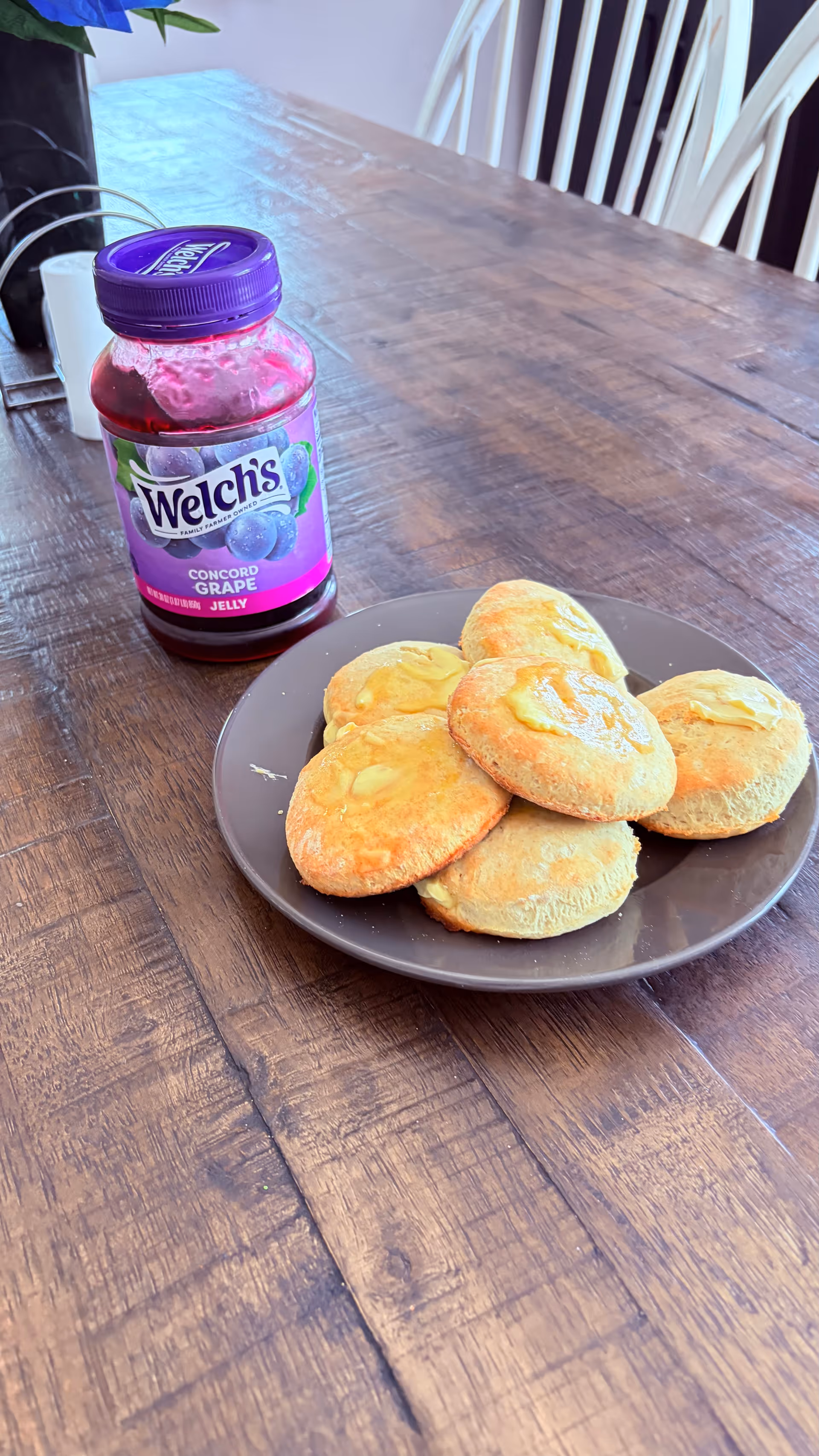 Wooden dining table with a plate of pastries and a jar of Welch's grape jelly.
