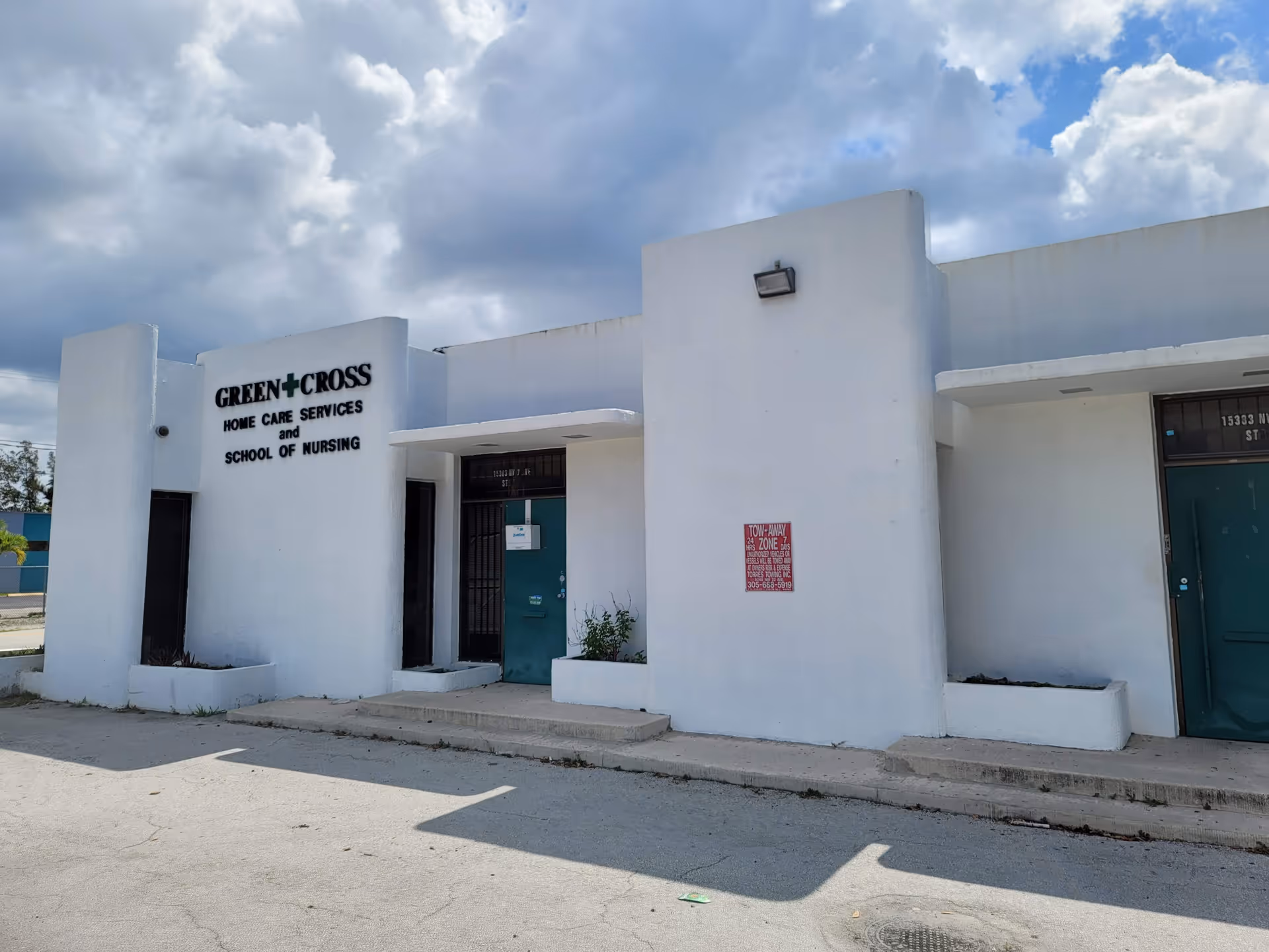 White building exterior with a Green Cross sign and multiple entry doors.