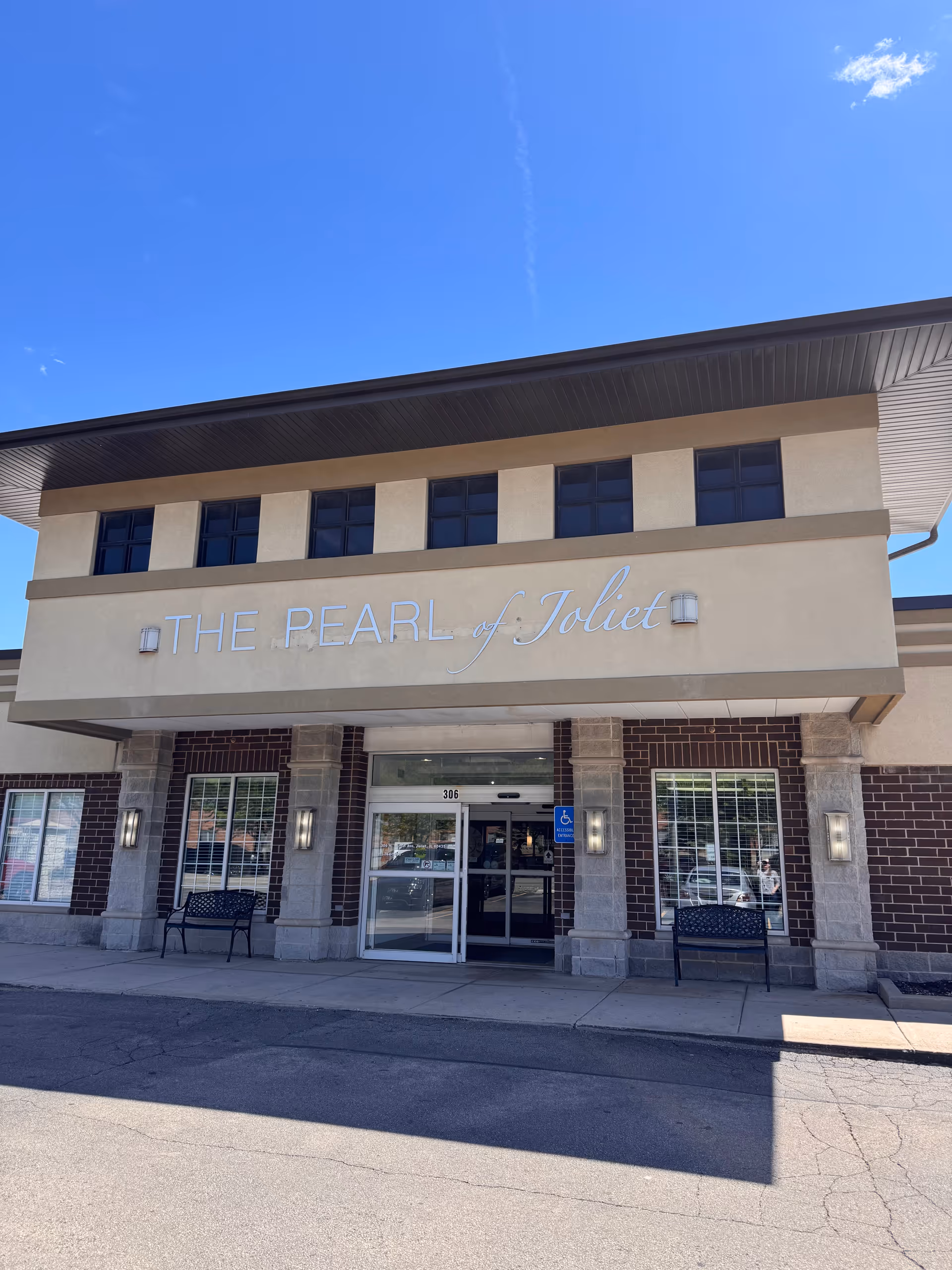 Front exterior of The Pearl of Joliet facility with glass doors and benches.