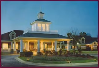 Exterior view of Azalea Estates of Fayetteville with a lit front porch and cupola