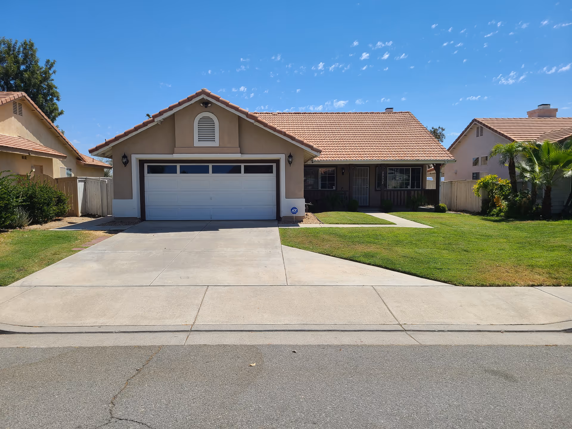 Front view of a tan house with a two-car garage and green lawn.