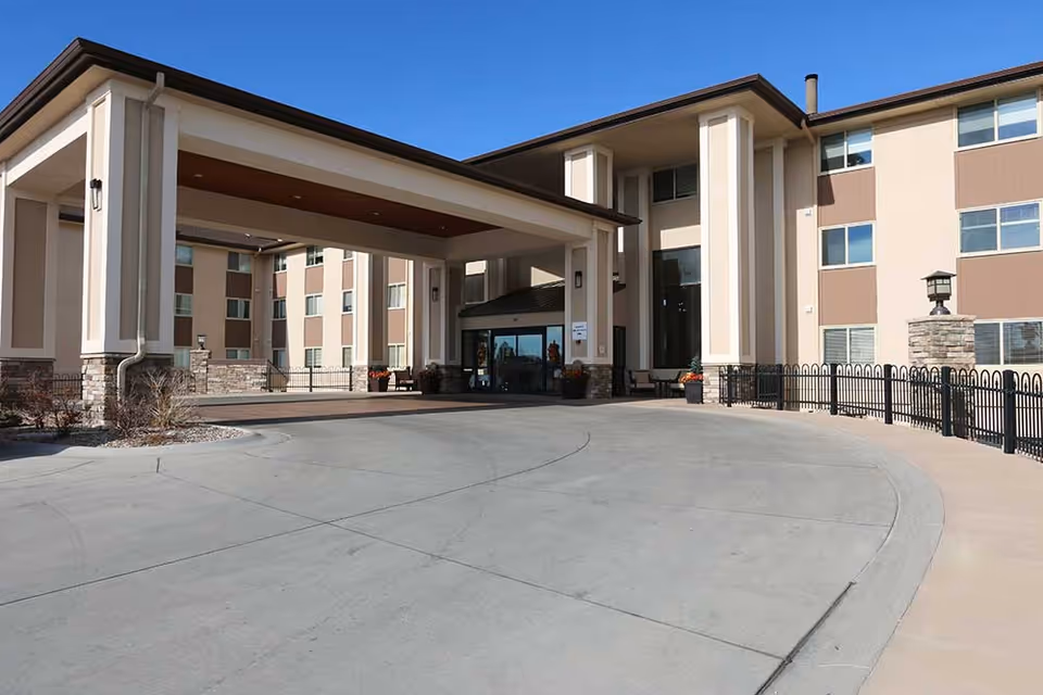 Front entrance of a multi-story senior living building with a covered porte-cochere and circular driveway.