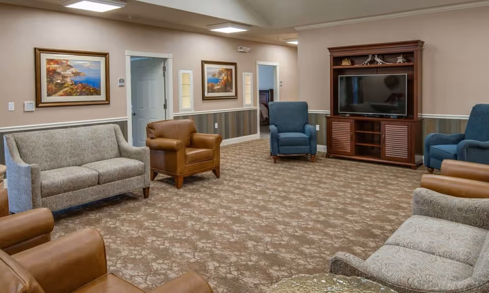 Spacious common sitting room with sofas and armchairs arranged around a TV cabinet and framed wall art.