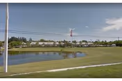Wide exterior view of Lake Worth Nursing Home campus with pond and flag.