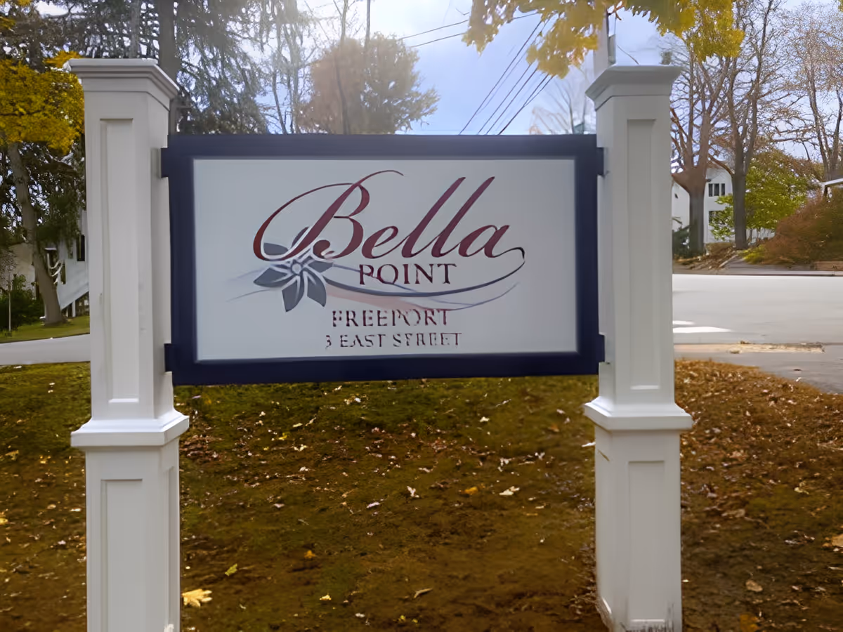 Outdoor sign for Bella Point Freeport located on 3 East Street, mounted on white posts with a background of trees and a street.