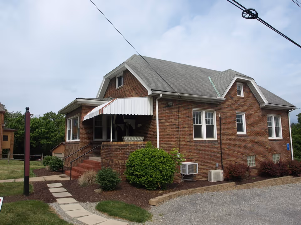 Brick senior living facility with a covered entrance, steps, and landscaped front yard.