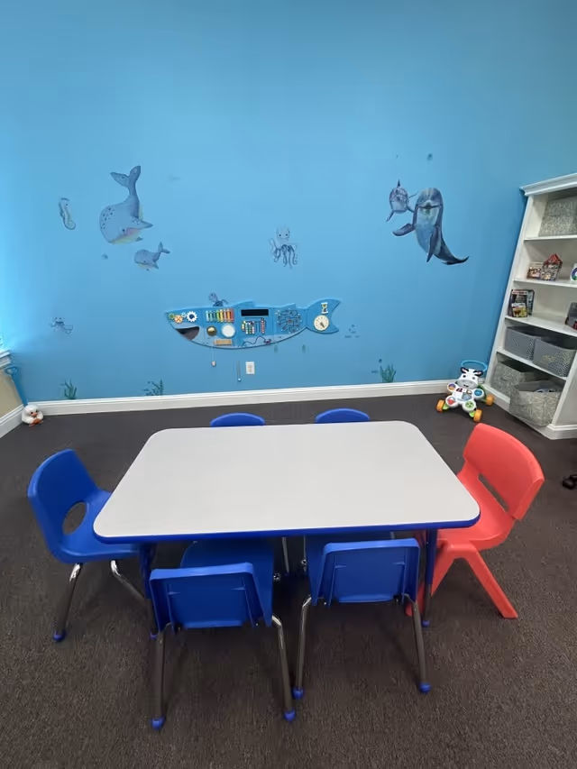 A blue-wall children's activity area in a senior facility with a small table and colorful chairs.
