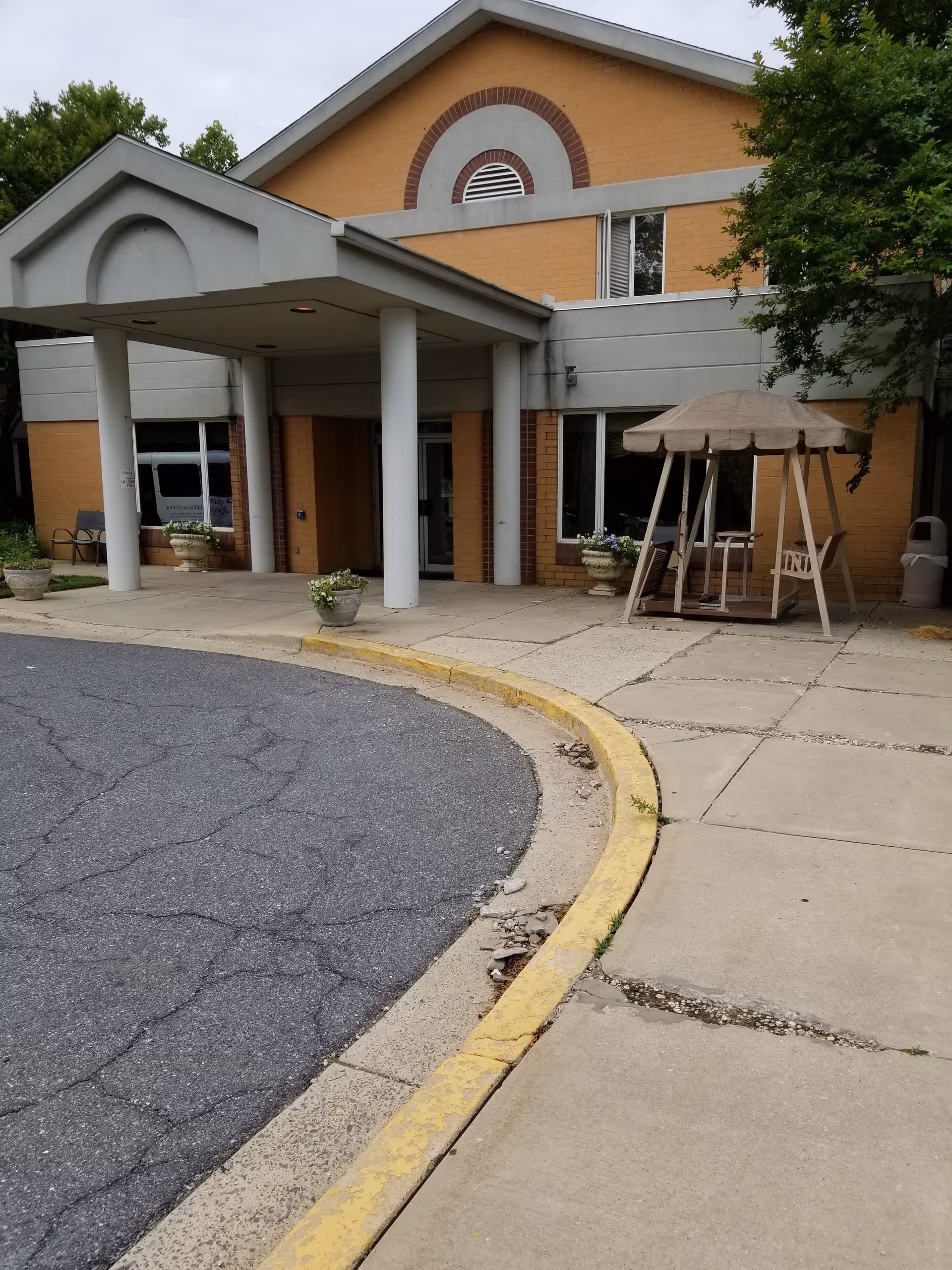 Exterior view of Adventist Healthcare Kingshire entrance with canopy, columns, and a swing bench.