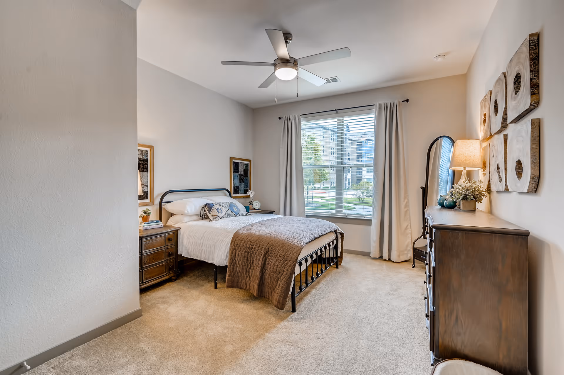 Cozy bedroom with a metal-framed bed, two dressers, nightstands, and a large window.