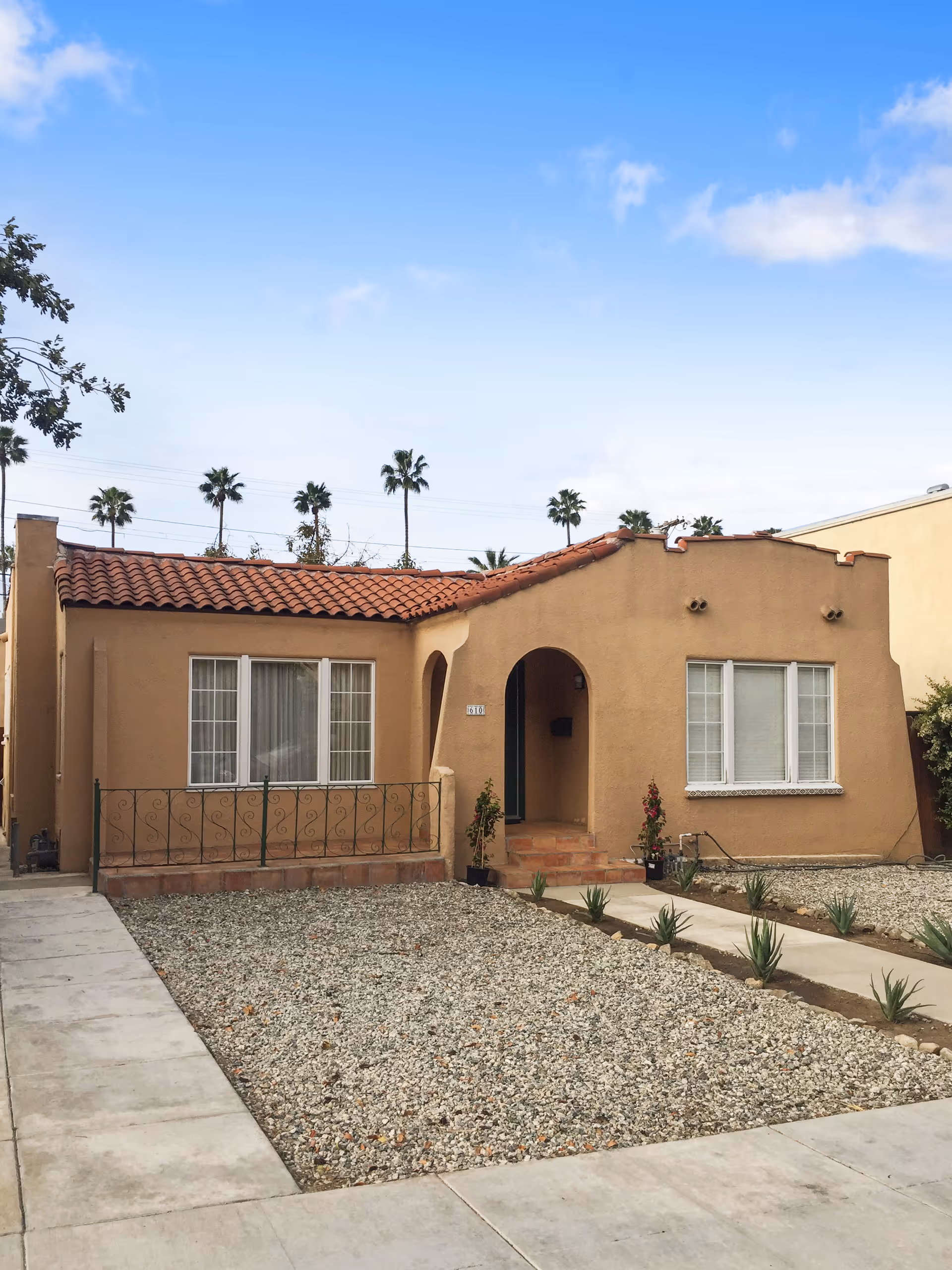 Single-story tan stucco senior living building with red tile roof, front entrance arch, desert landscaping.
