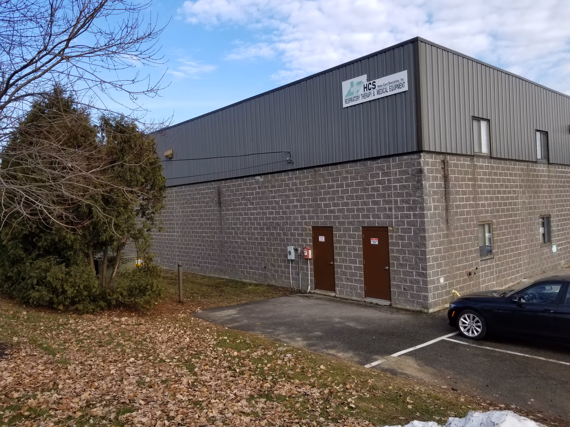 Exterior view of a gray brick and metal building with two doors and a parked car.