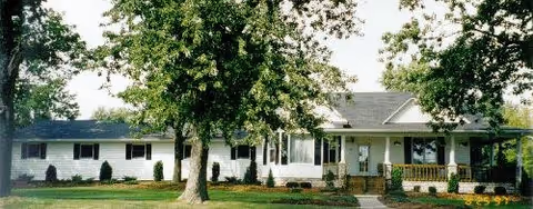 Front exterior of a single-story senior living building with trees and a porch.