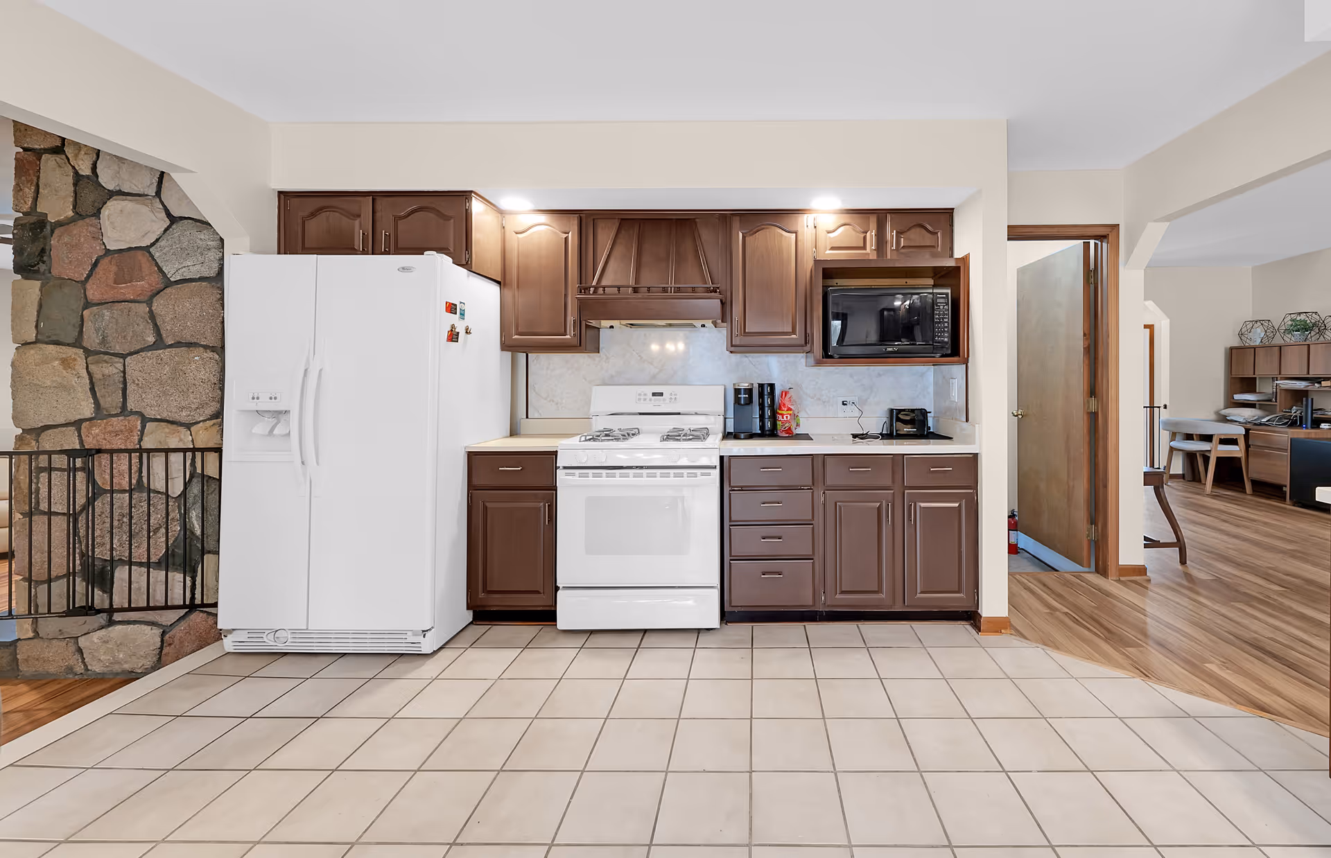 Kitchen with white appliances, brown cabinets, and a stone wall in a senior living facility.