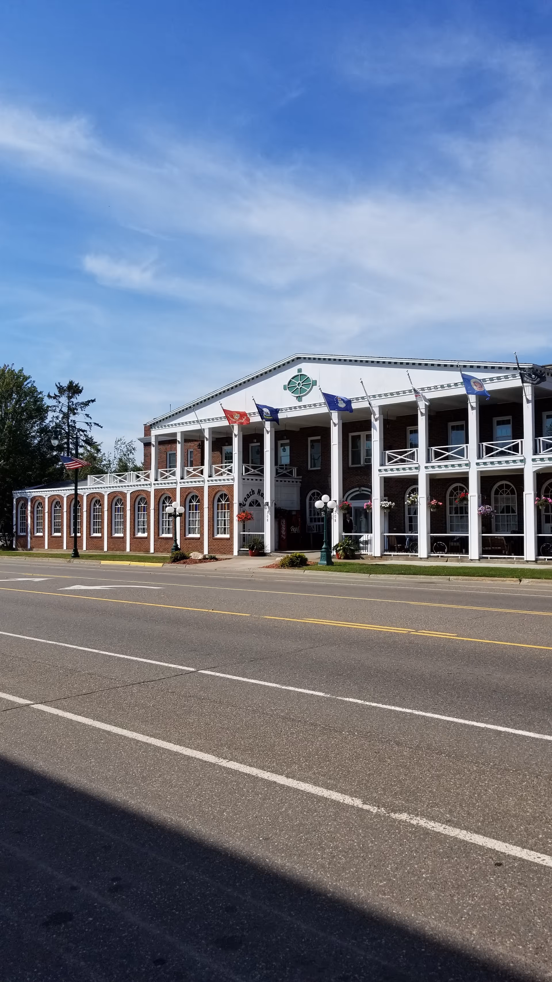 Two-story brick senior living facility with white columns, arches, and flags along a street.