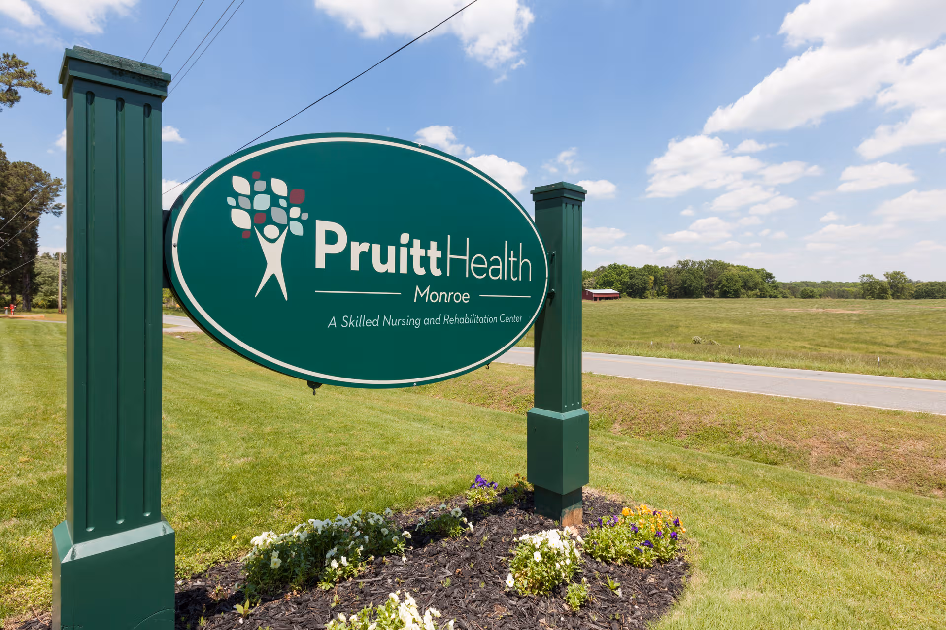 Green PruittHealth Monroe sign on a manicured lawn with road and blue sky
