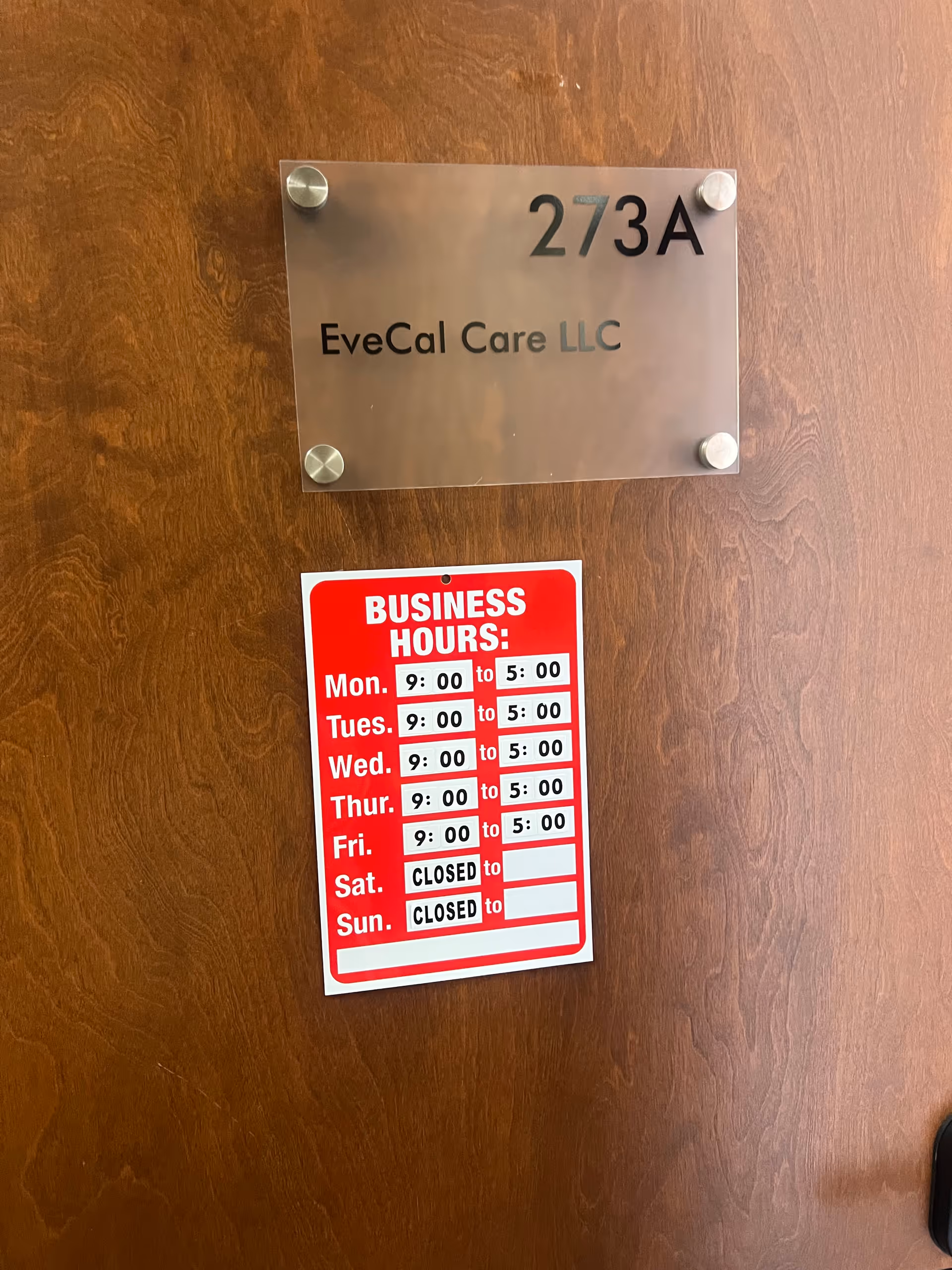 Metal plaque with EveCal Care LLC and a red business hours sign on a wooden door.