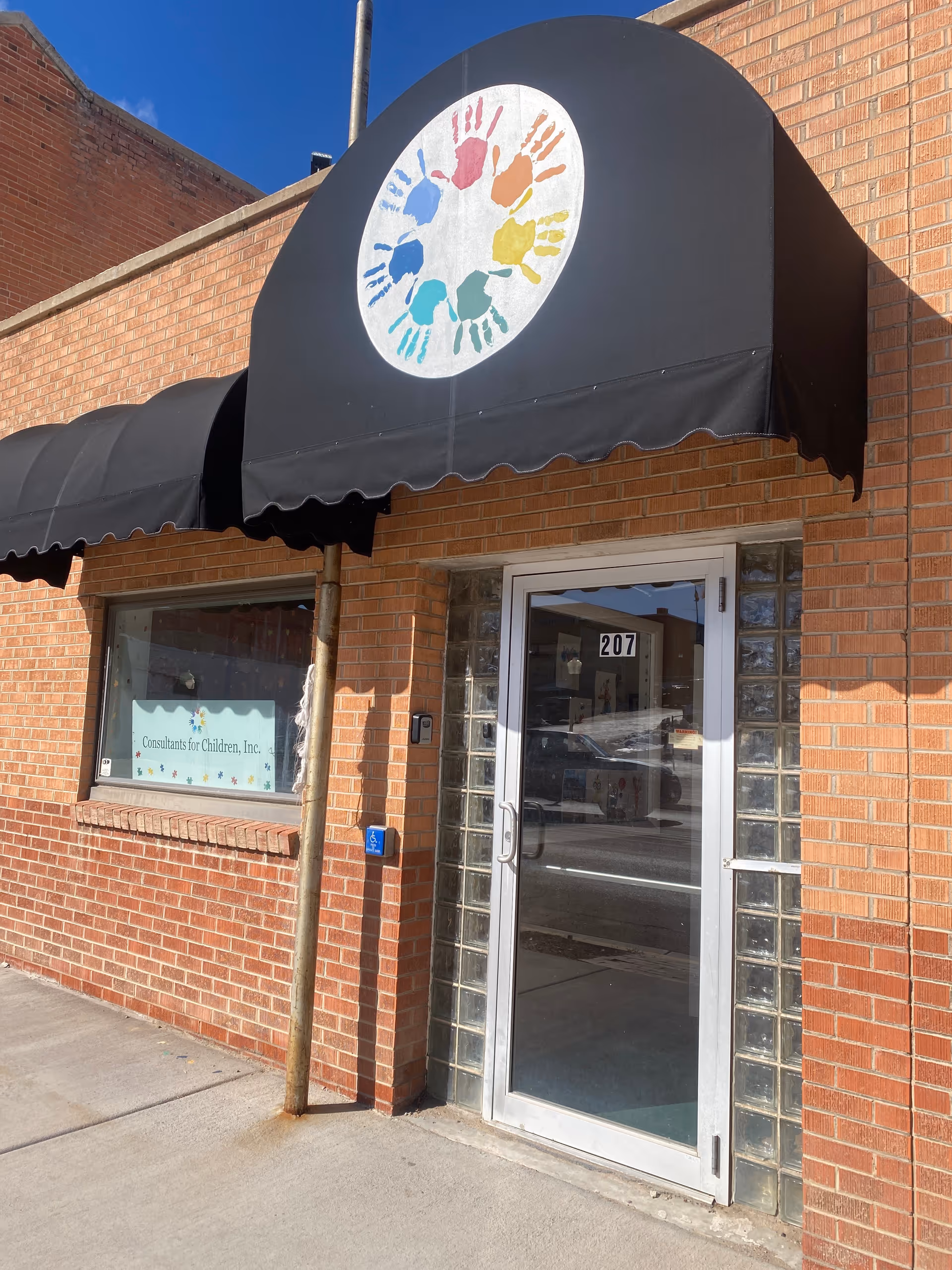 Entrance to Consultants for Children, Inc. Trinidad, brick building with black awning and colorful logo.
