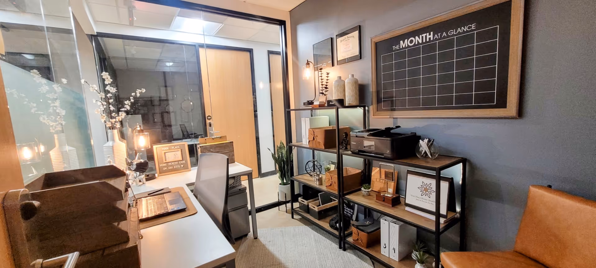 Compact office reception area with desk, shelving, calendar board, and warm decor.