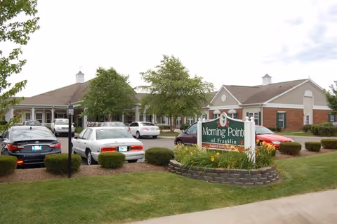 Front exterior of Morning Pointe of Franklin with parked cars and a landscaped sign.