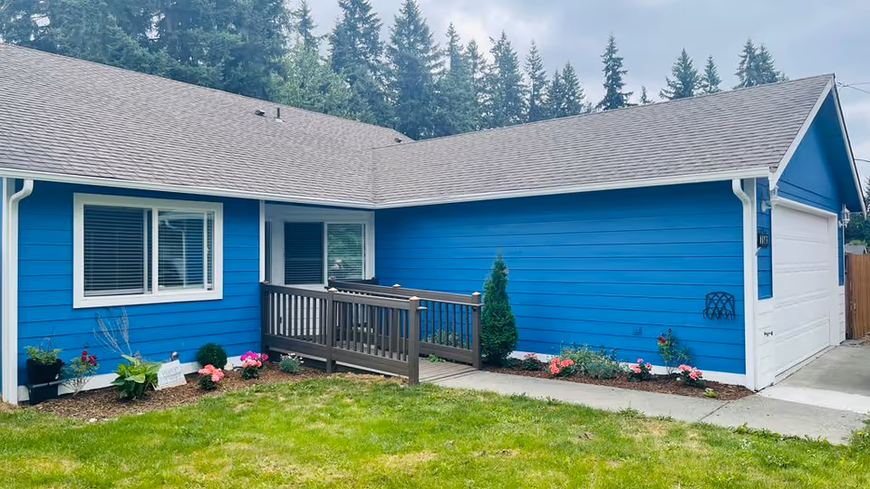 Blue single-story building with a small ramp and flower-filled front yard.