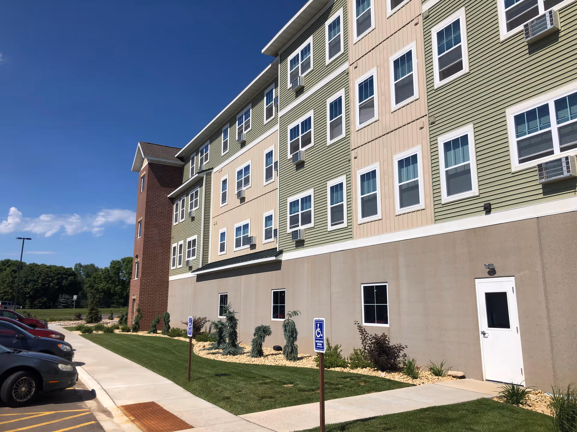 Exterior view of a multi-story senior living building with green-beige siding and parking.